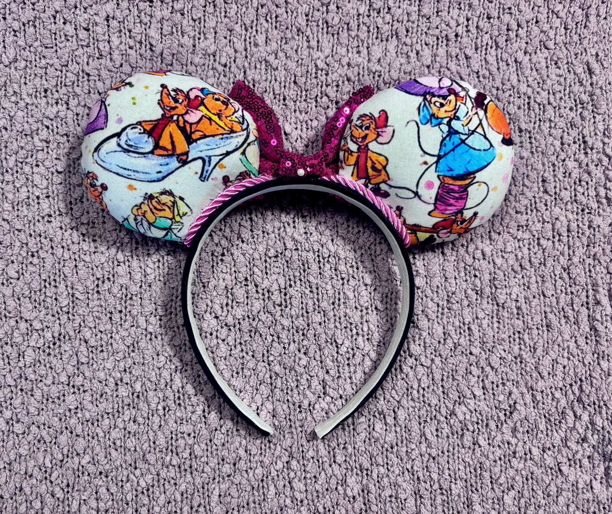 Back view of mouse ears. Handmade and ready to ship Sewing Mice mouse ears with the fabric on both the front and back. The headband is black universal sized and fits most. The set has a hot pink sequin bow with pink twisted trim along the inner mouse ears. Item is shown on a lavender fluffy background.