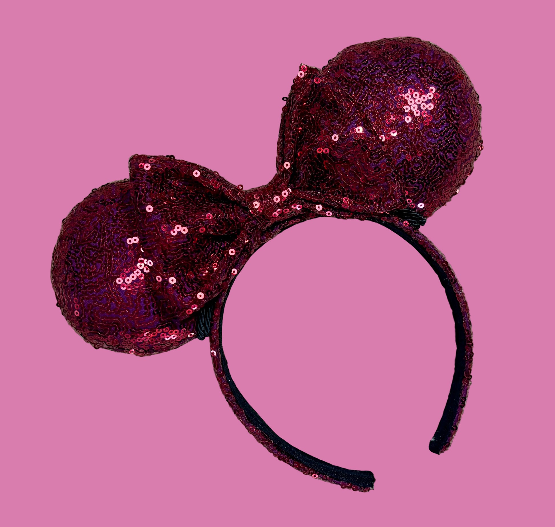 A pair of sequined ears headband with a bow, featuring deep magenta sequins on a black headband.