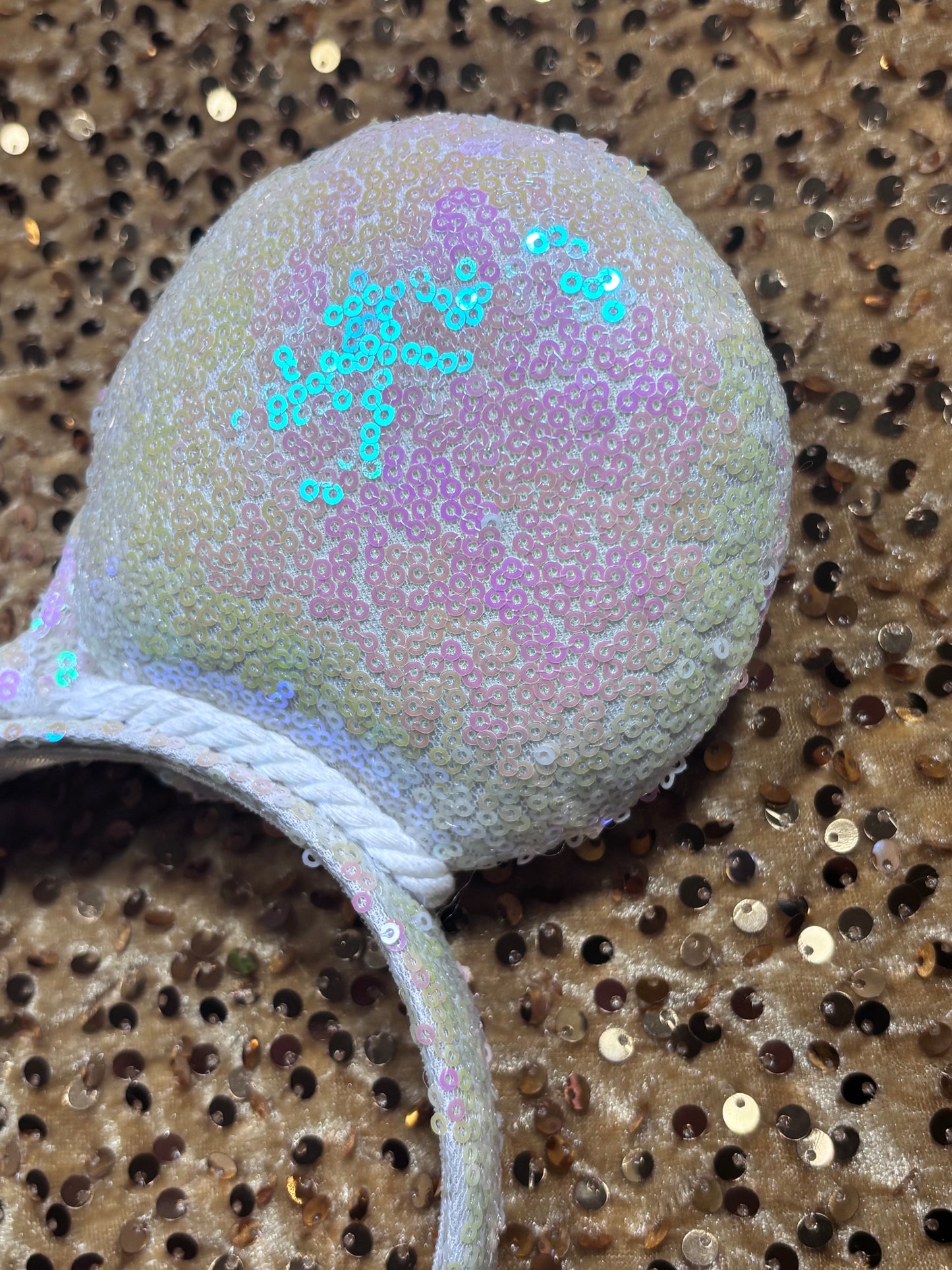 White Iridescent mouse ears with the fabric on both the front and back. The fabric is on the headband as well and is universal sized and fits most. The set has a matching iridescent bow sequin bow. Item is shown on a gold sequin background. back view.
