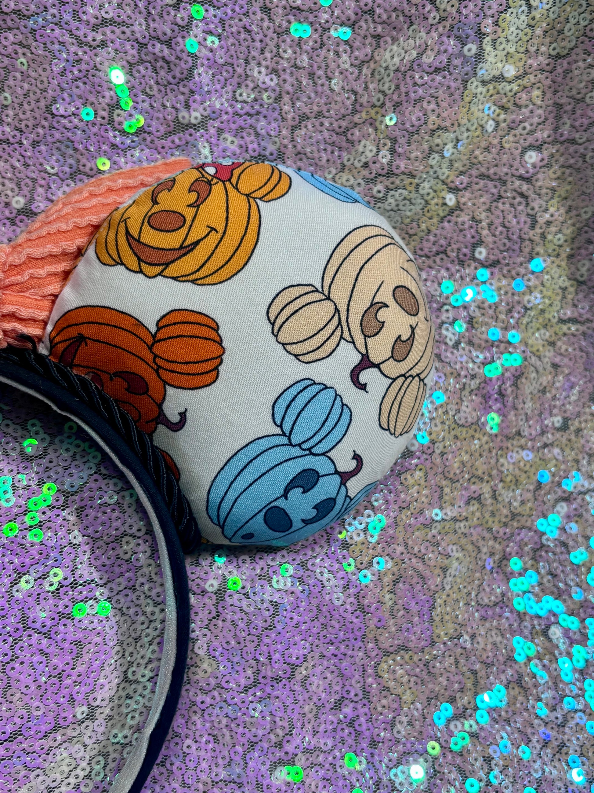 Mouse Ears with pumpkins on them on a black headband with an orange waffle print bow and white glitter background