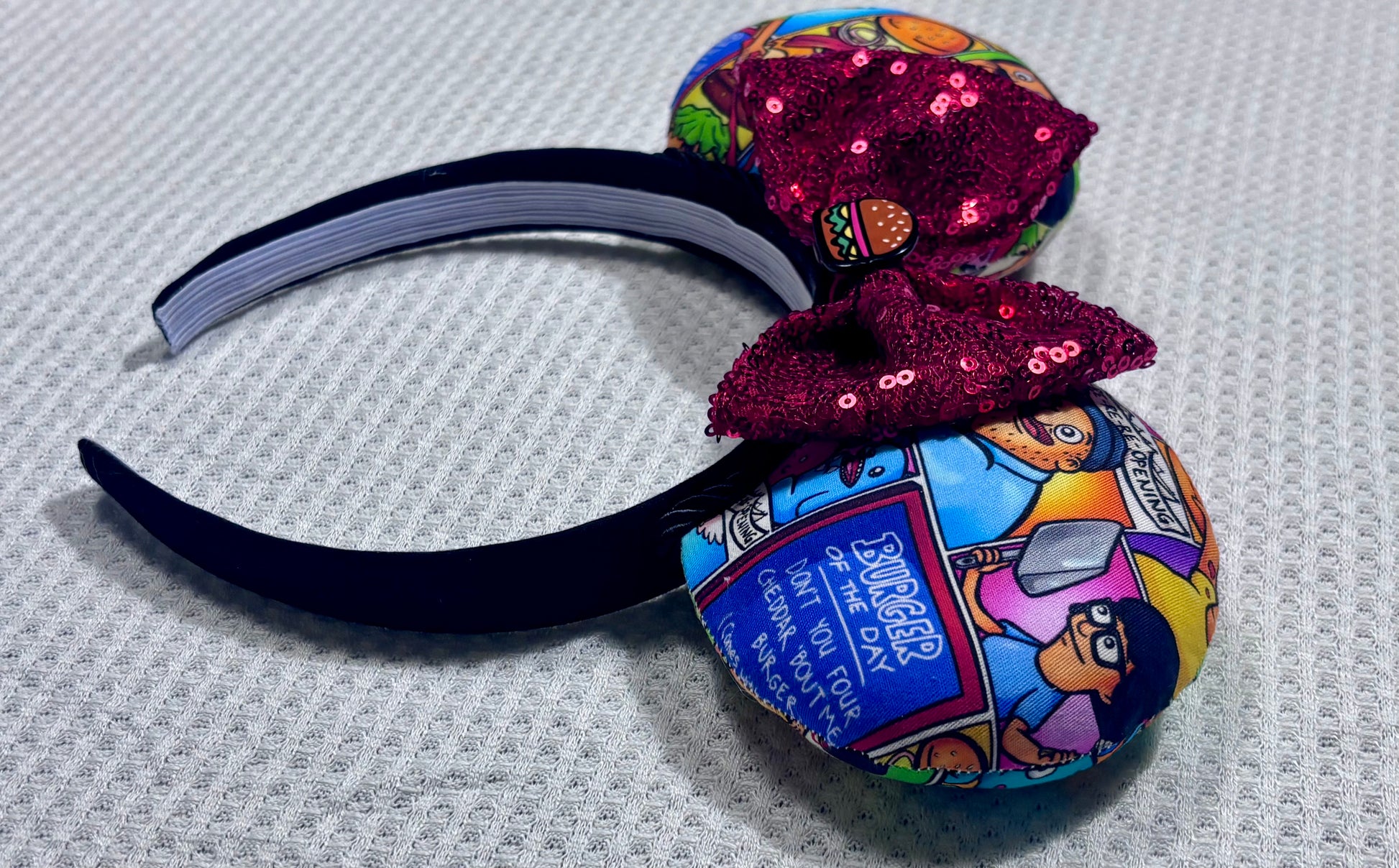 Handmade and ready to ship Belcher and friends mouse ears with the fabric on both the front and back. The headband is black universal sized and fits most. The set has a red sequin bow with a burger embellishment on the middle. Item is shown on a white background.