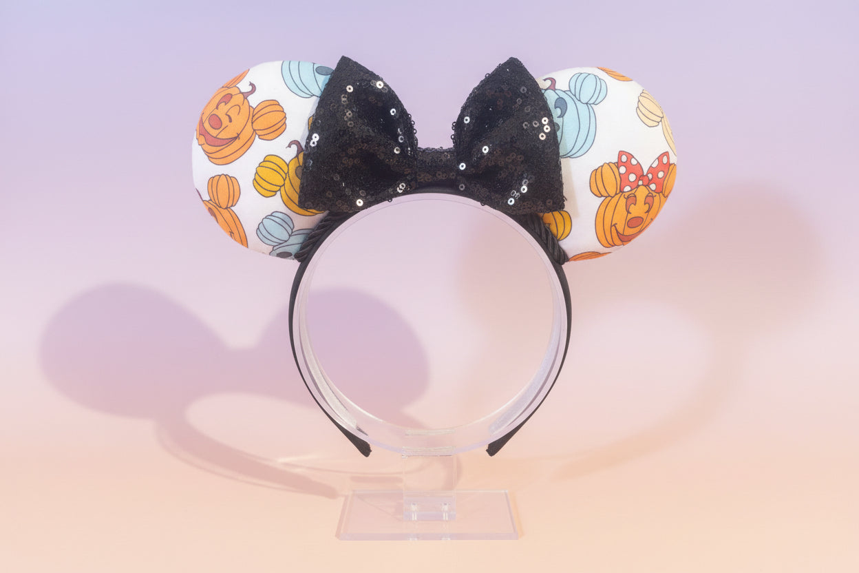 Halloween-themed with mouse pumpkins on the Mouse ears with a black bow and black twisted trim on a black headband. Shown on a stand against a light background