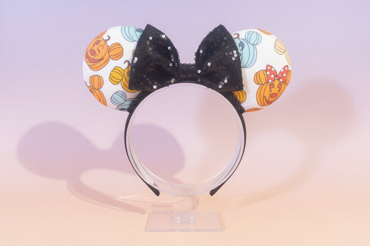 Halloween-themed with mouse pumpkins on the Mouse ears with a black bow and black twisted trim on a black headband. Shown on a stand against a light background