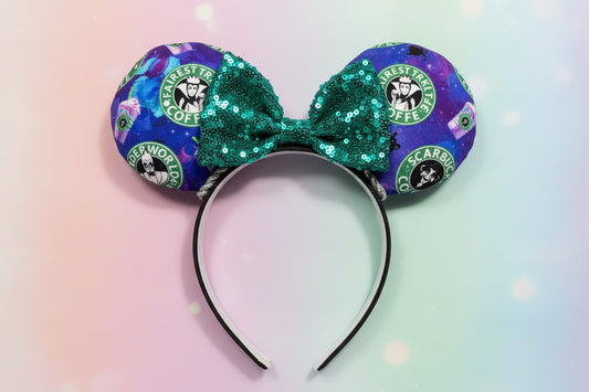 Coffee themed mouse ears with cartoon villains on them with a green bow and silver twisted trim. Shown on a gradient background