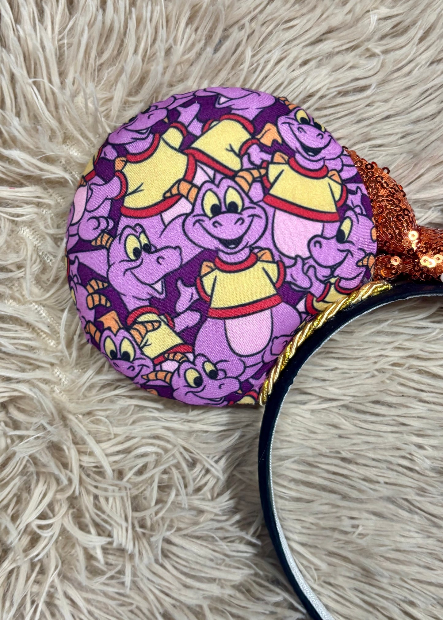 A close-up of a round headband featuring a purple and yellow cartoon dragon pattern, resting on a beige shag rug.
