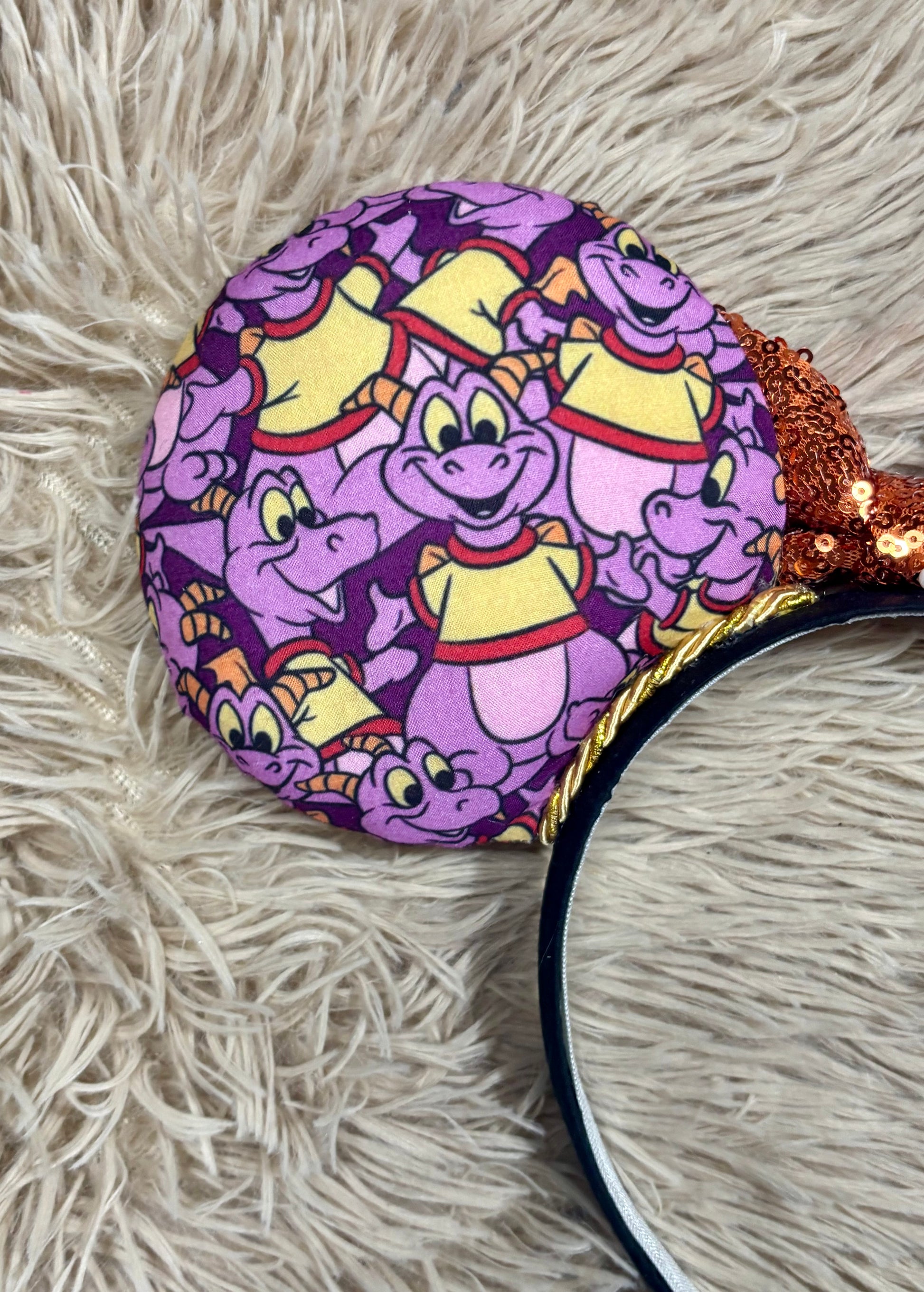 A close-up of a round headband featuring a purple and yellow cartoon dragon pattern, resting on a beige shag rug.