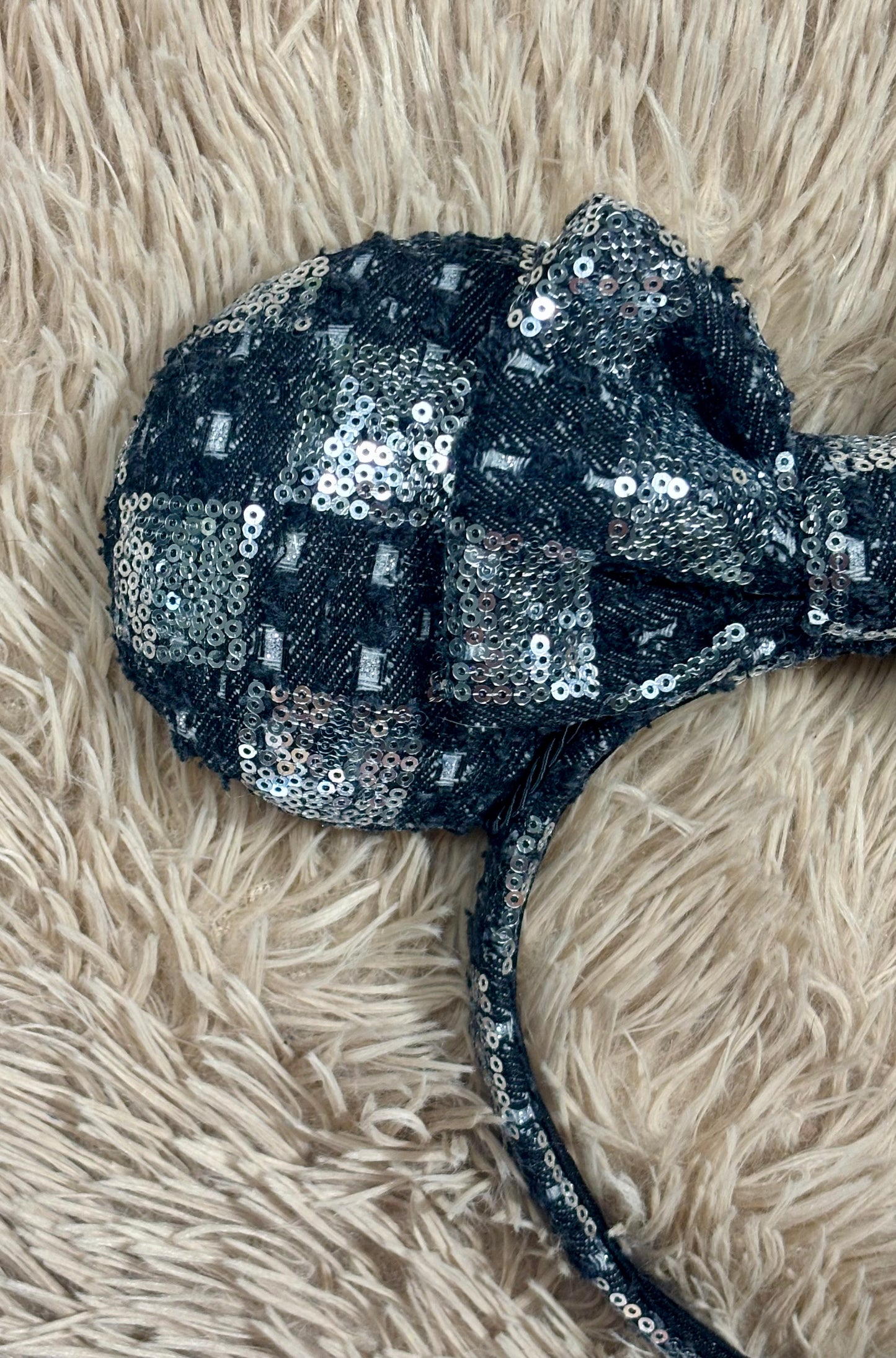 A black and silver checkered sequined headband with large bow ears. Close up of front of mouse ear.