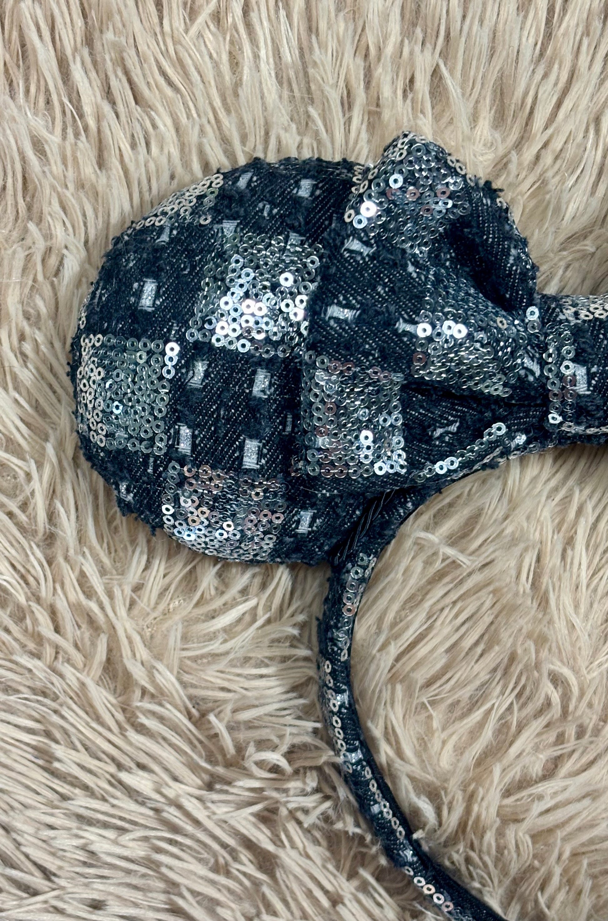 A black and silver checkered sequined headband with large bow ears. Close up of front of mouse ear.
