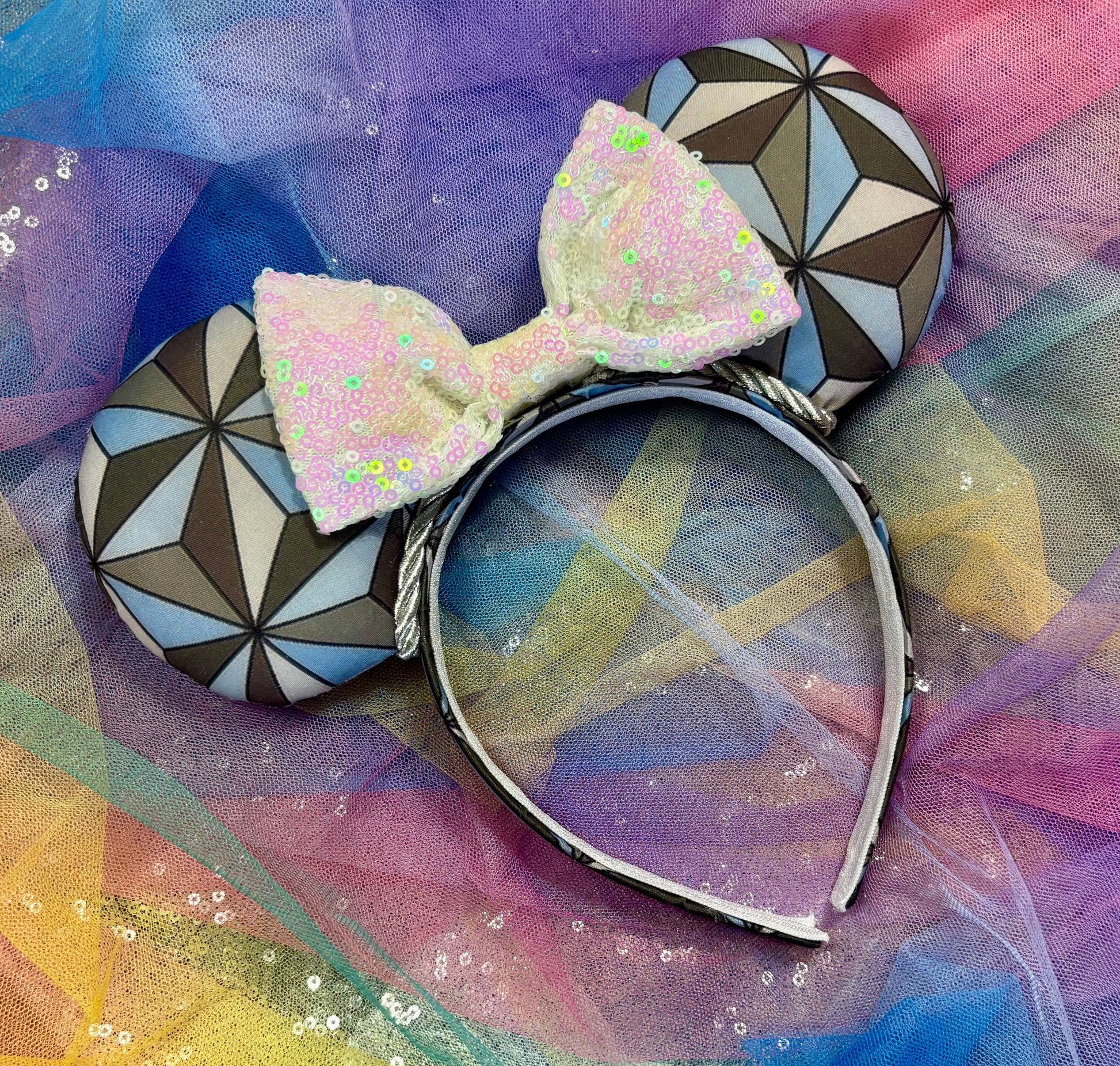 Decorative headband with geometric design and white iridescent bow on a colorful fabric background.