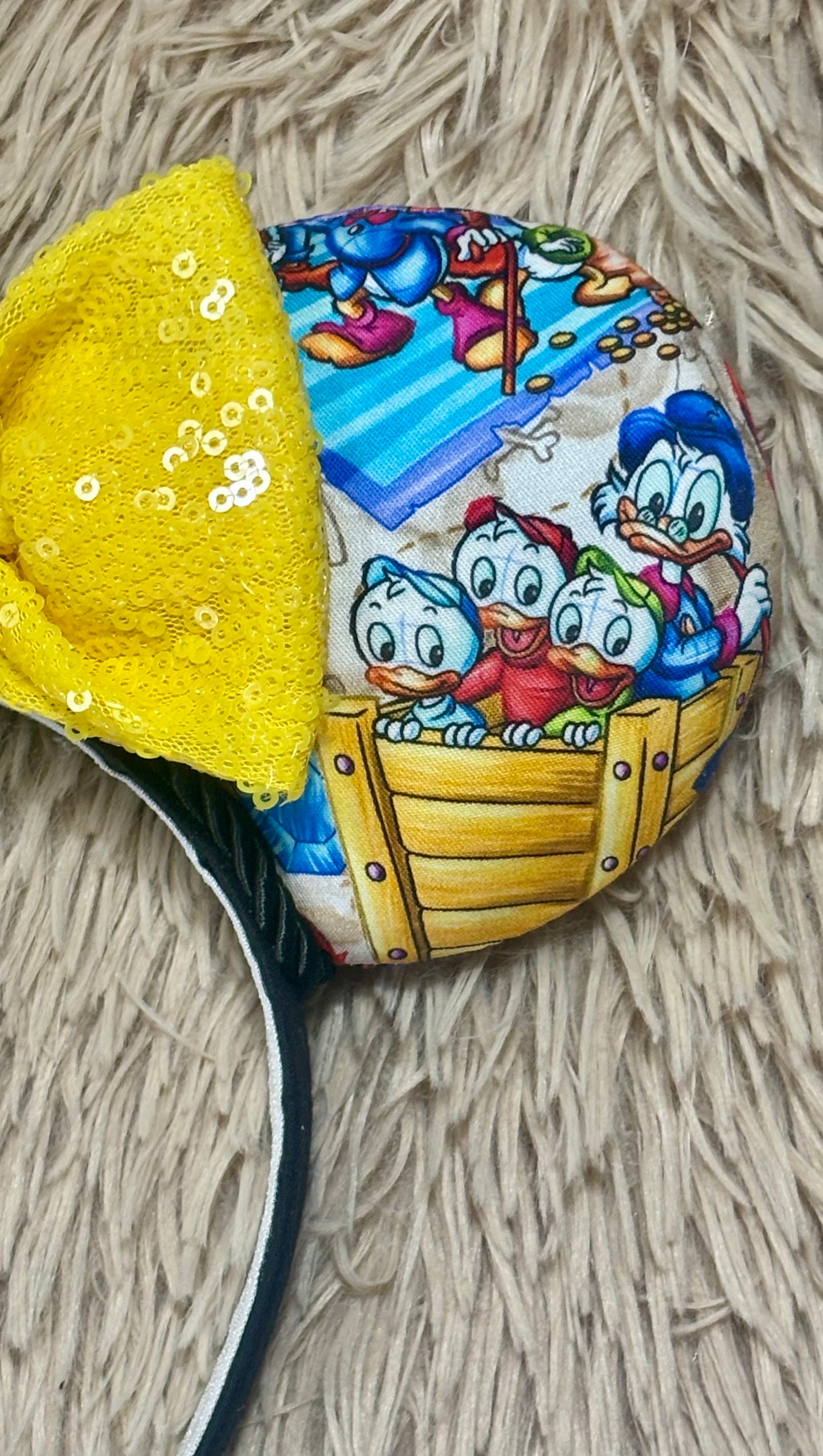 A close-up of headband featuring a colorful cartoon print of Duck characters paired with a bright yellow sequined fabric section.
