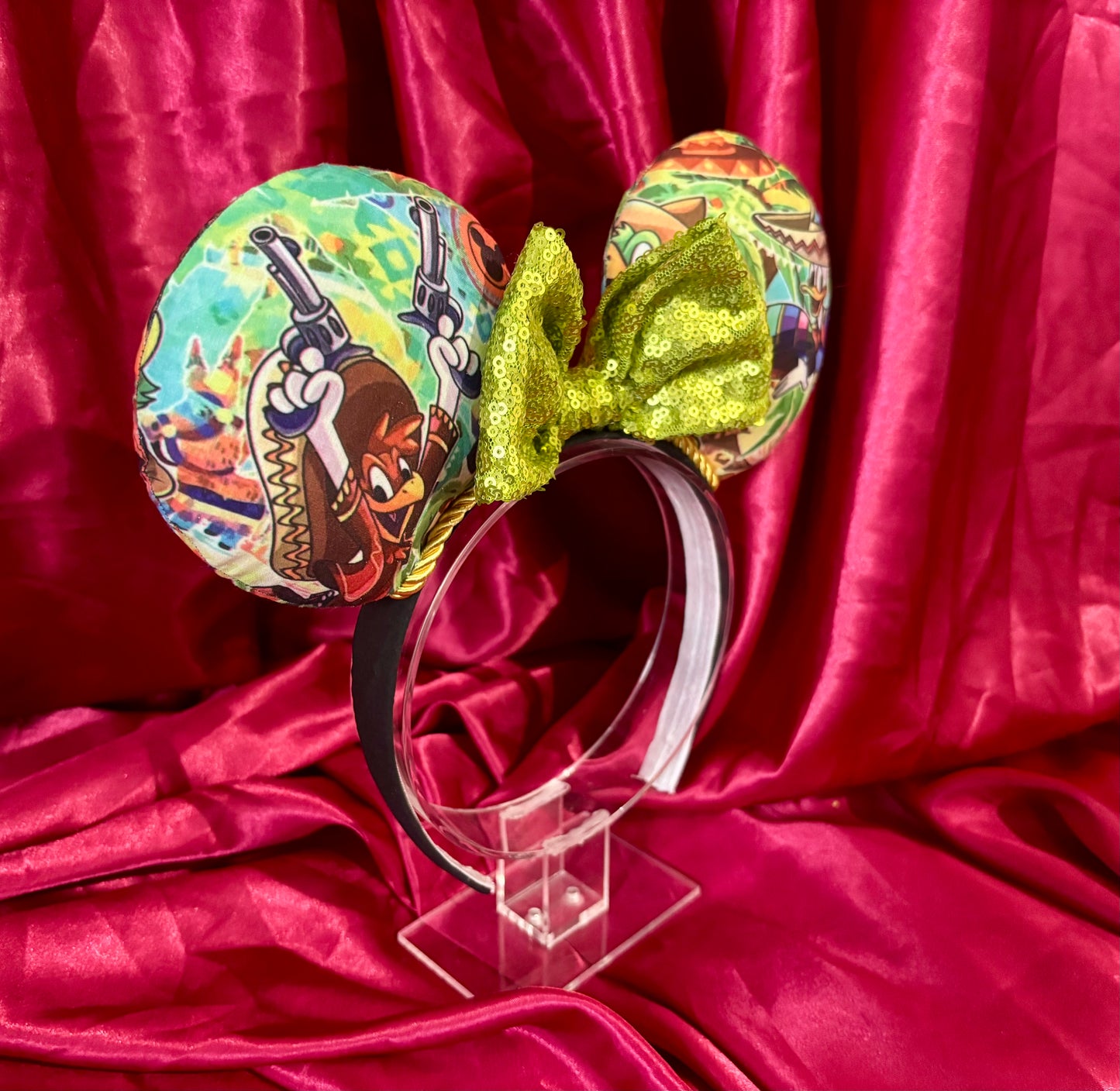Side view. Colorful Handmade mouse ears with a green bow on a red satin background with duck cartoon images on the ears
