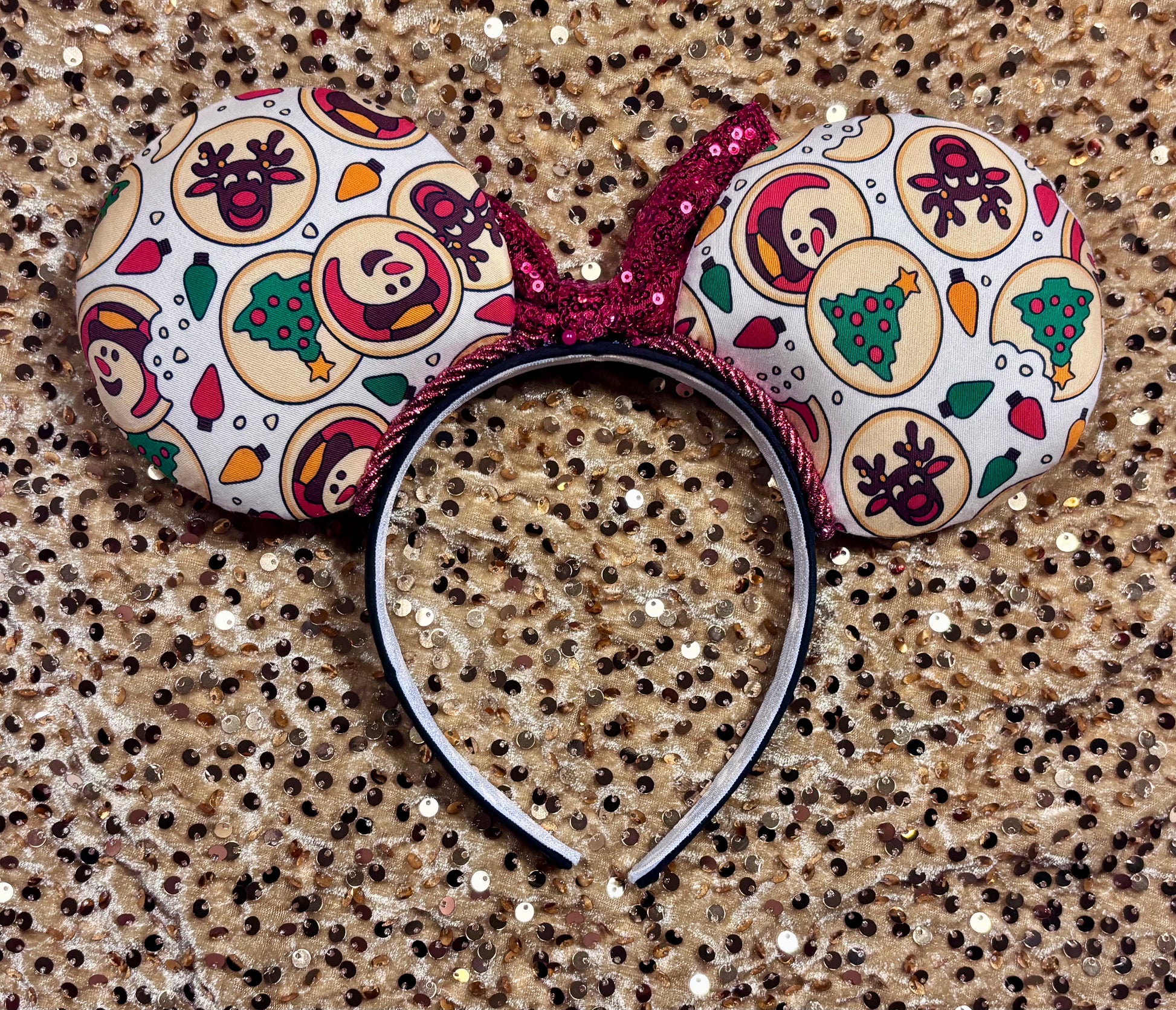 Christmas Sugar Cookie mouse ears with the fabric on both the front and back. The headband is black universal sized and fits most. The set has a red sequin bow. Item is shown on a gold sequin background