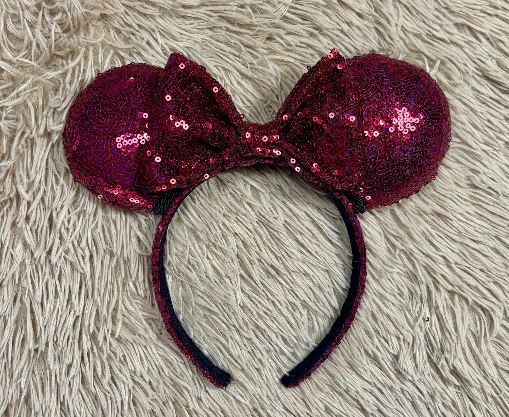 A pair of sequined ears headband with a bow, featuring deep magenta sequins on a black headband.