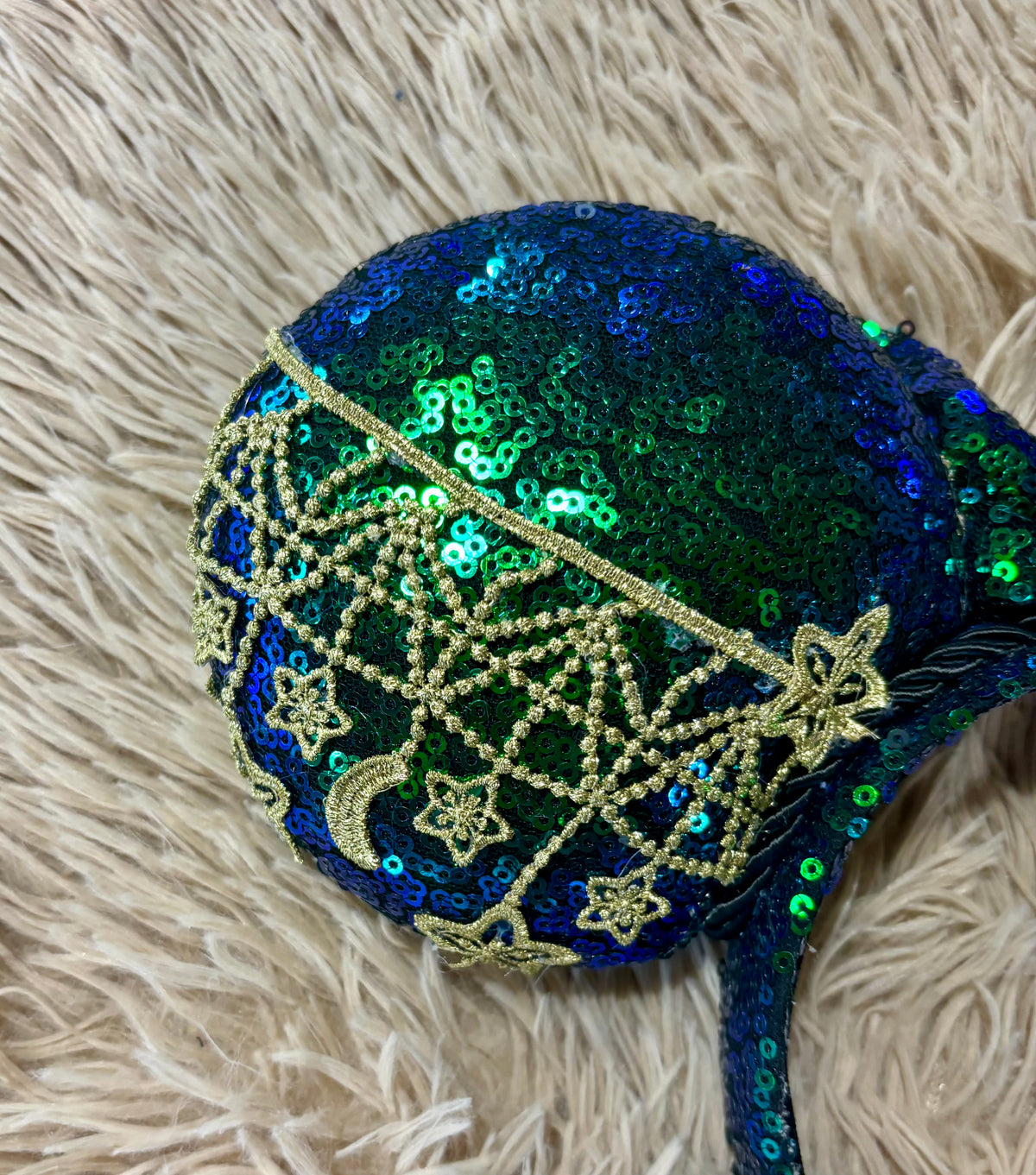 A pair of blue and green iridescent ear headband featuring dark blue and green sequins with gold embroidered stars, moons, and web patterns.