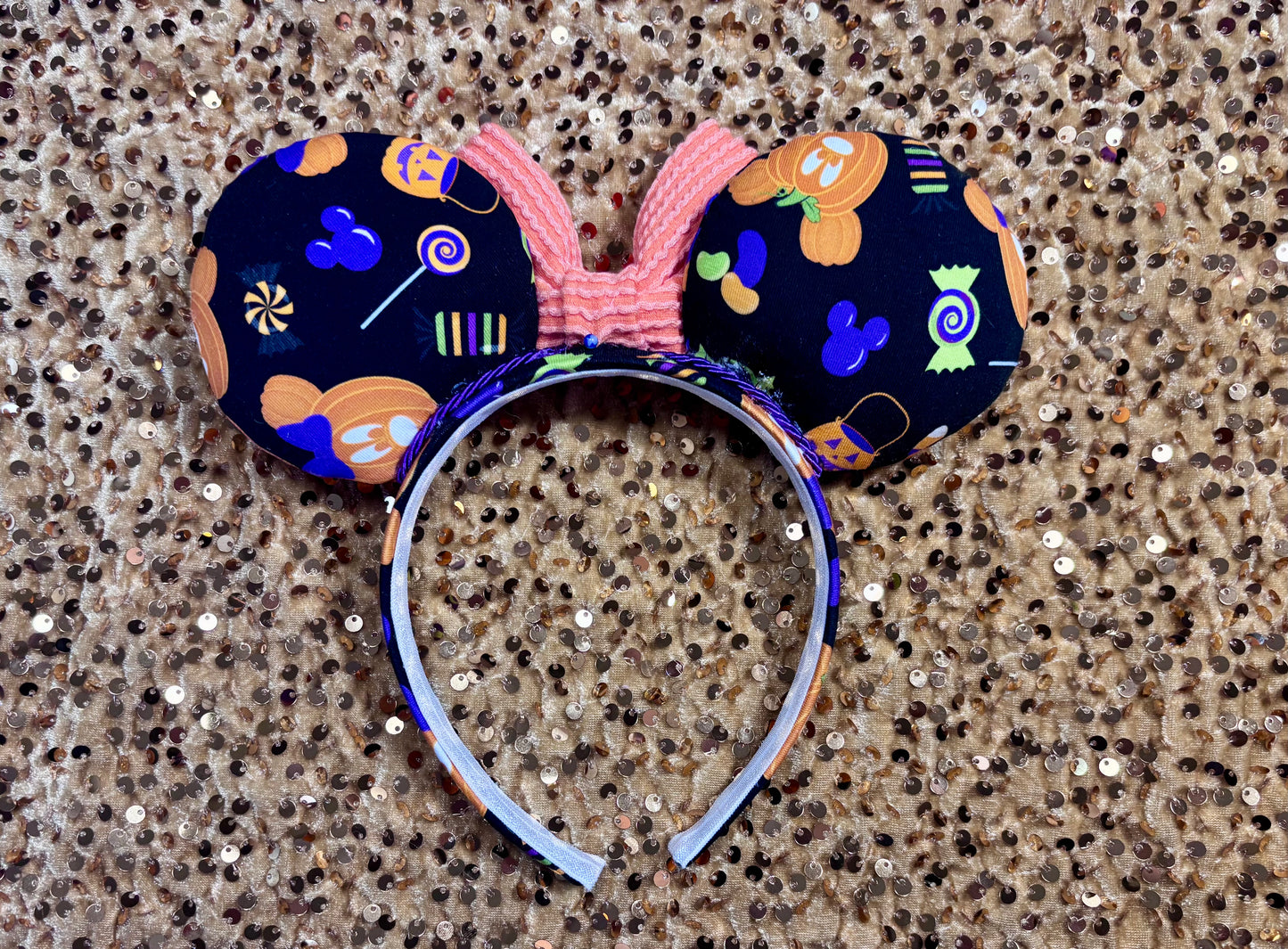 Custom ears with an orange bow center on a glittery surface. Back view of custom ear