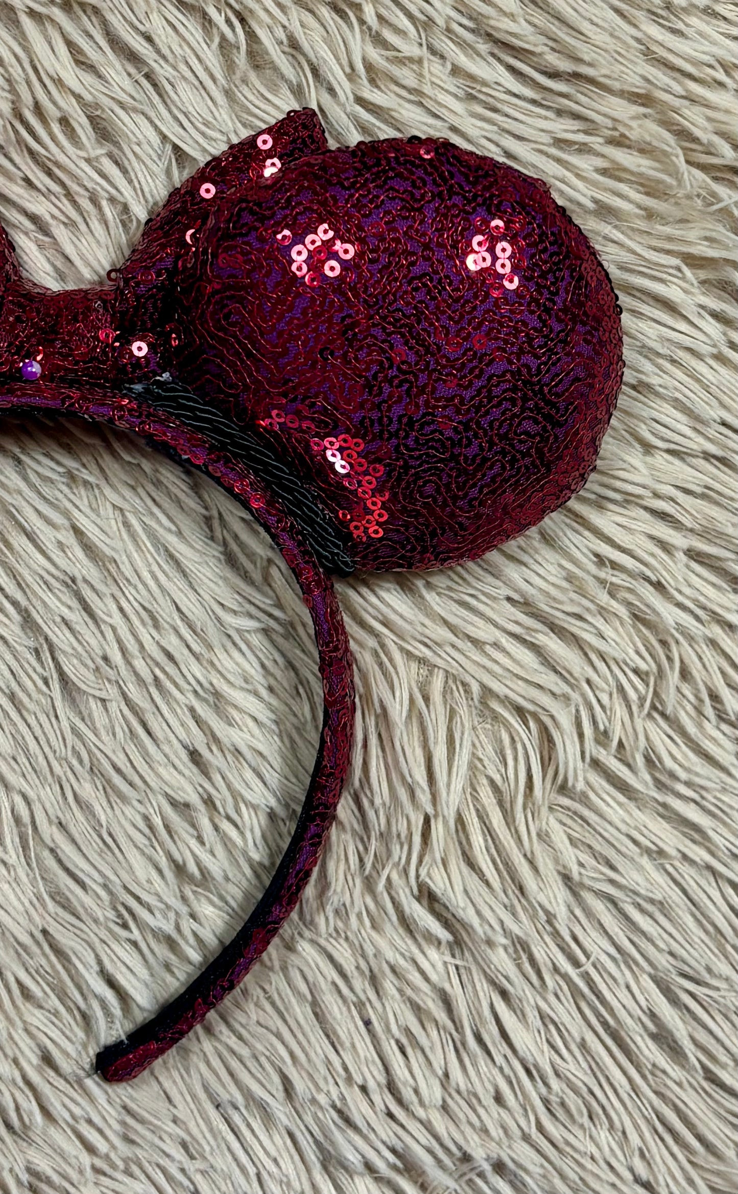 A pair of sequined ears headband with a bow, featuring deep magenta sequins on a black headband.