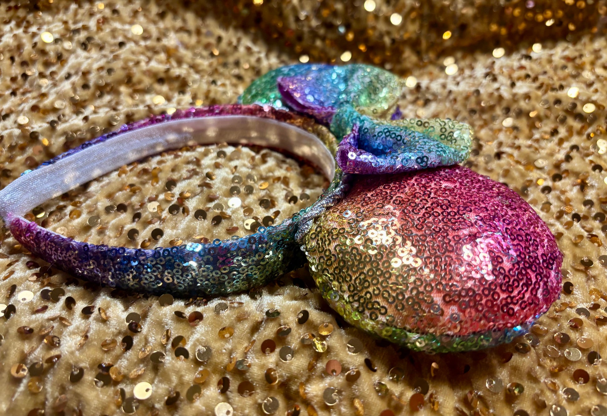 Handmade and ready to ship. Mouse ears with rainbow fabric are on the front and back of mouse ears along with the headband with a matching rainbow sequin bow. Shown on a gold sequin background.