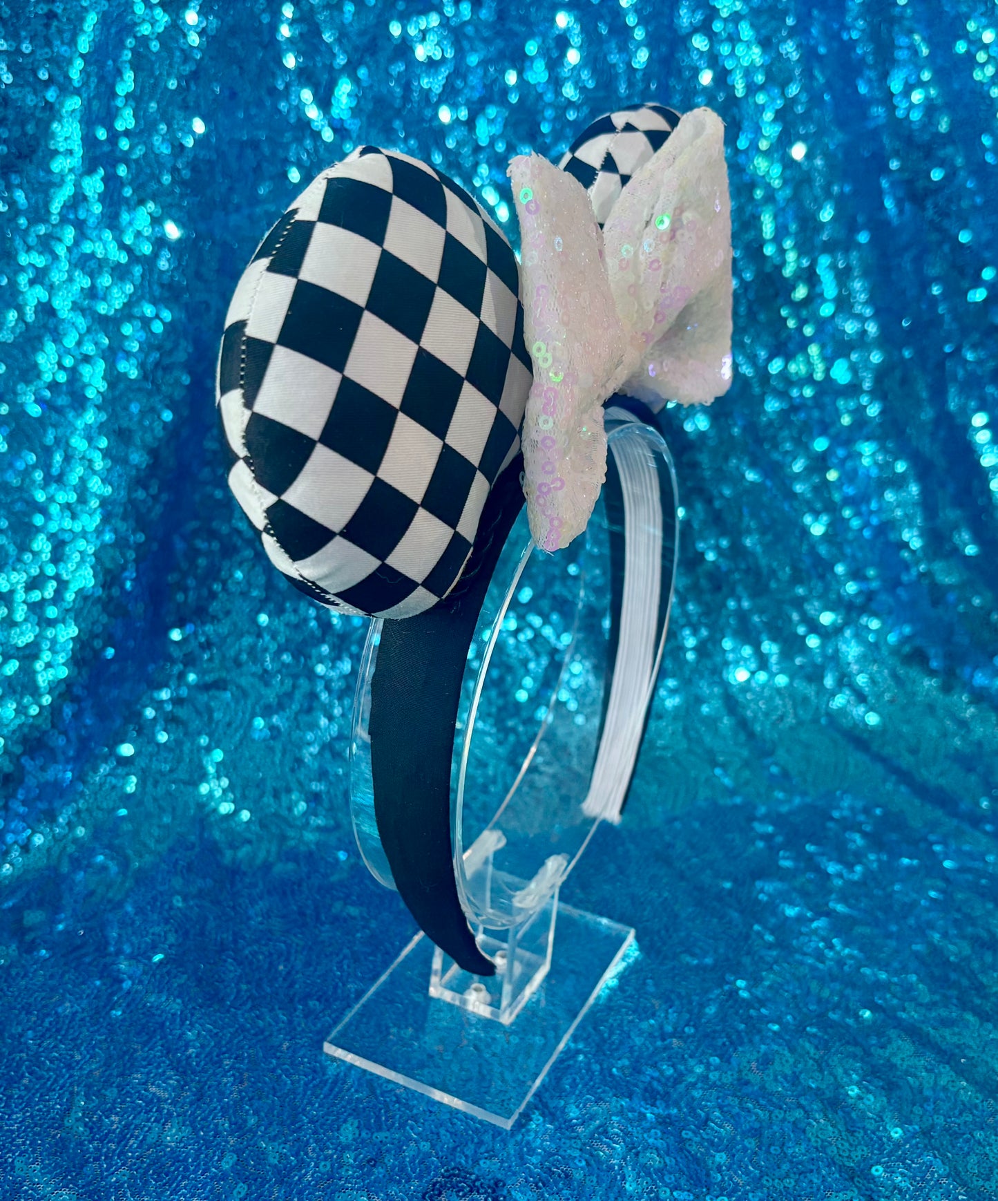 The other side view of Checkered bow headband on a clear stand against a blue glittery background
