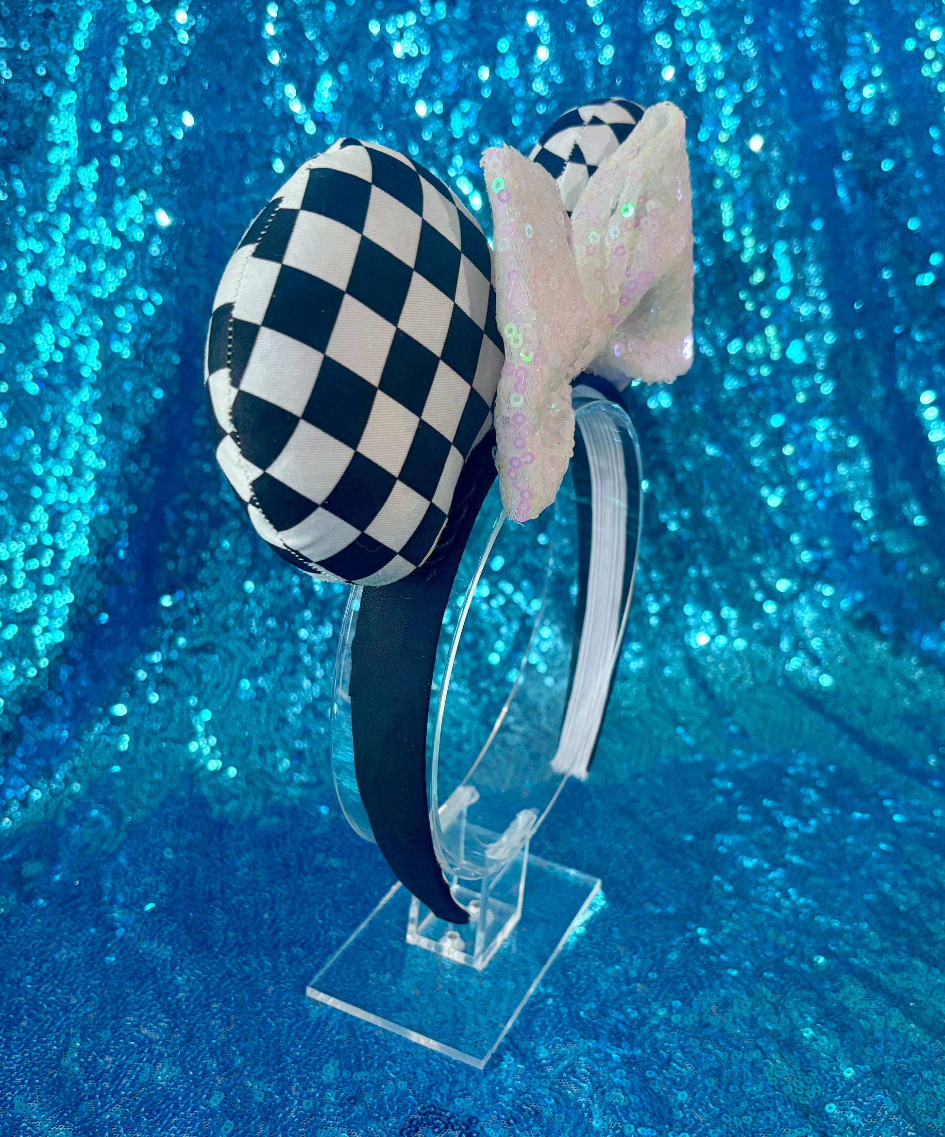 The other side view of Checkered bow headband on a clear stand against a blue glittery background