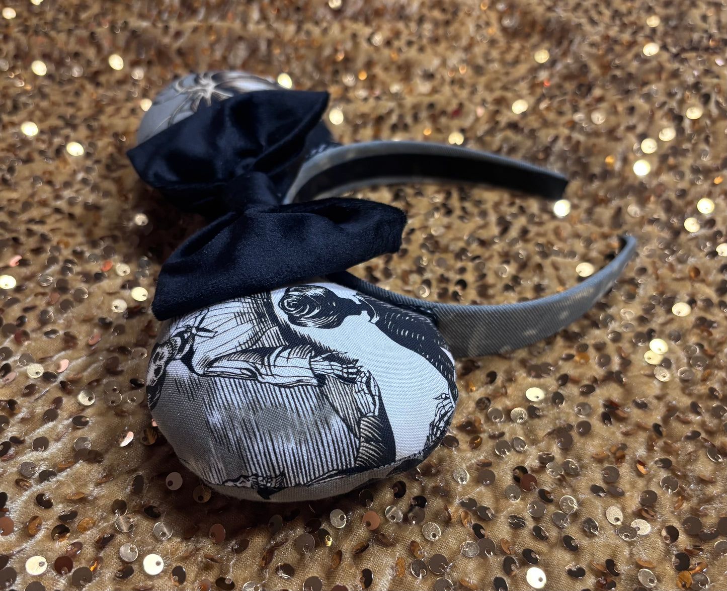 Handmade and one of a kind Halloween mouse ears with the fabric on both the front and back. Skeleton ghost having a seance on one side and an evil pumpkin on the other ear. The headband is grey and universal sized and fits most. The set has a black velvet bow. Item is shown on a gold sequin background.