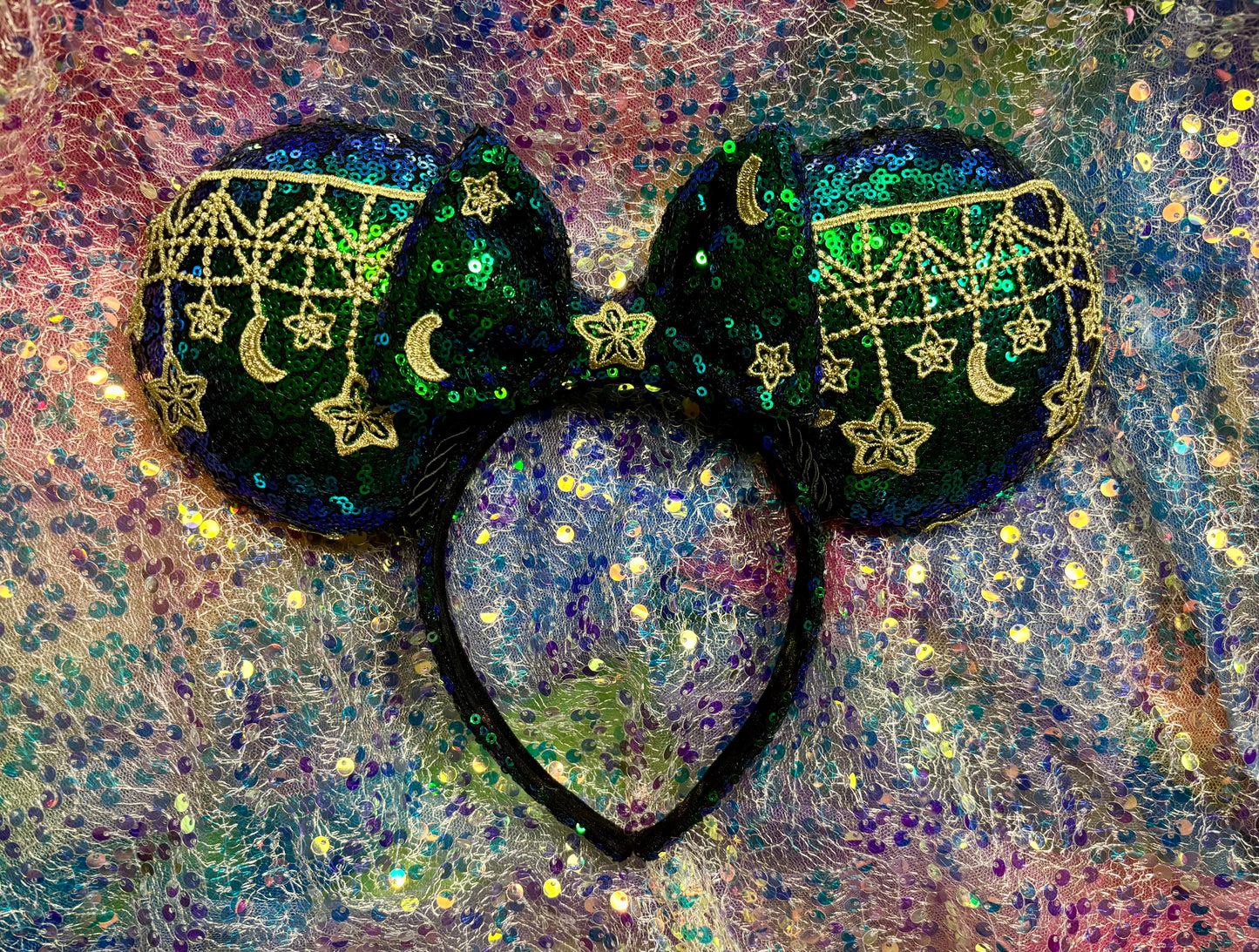 Mouse Ear headband that is a Handmade Iridescent blue and green sequins with gold sun, moon and stars attached to them. bow with star and moon patterns on a glittery background