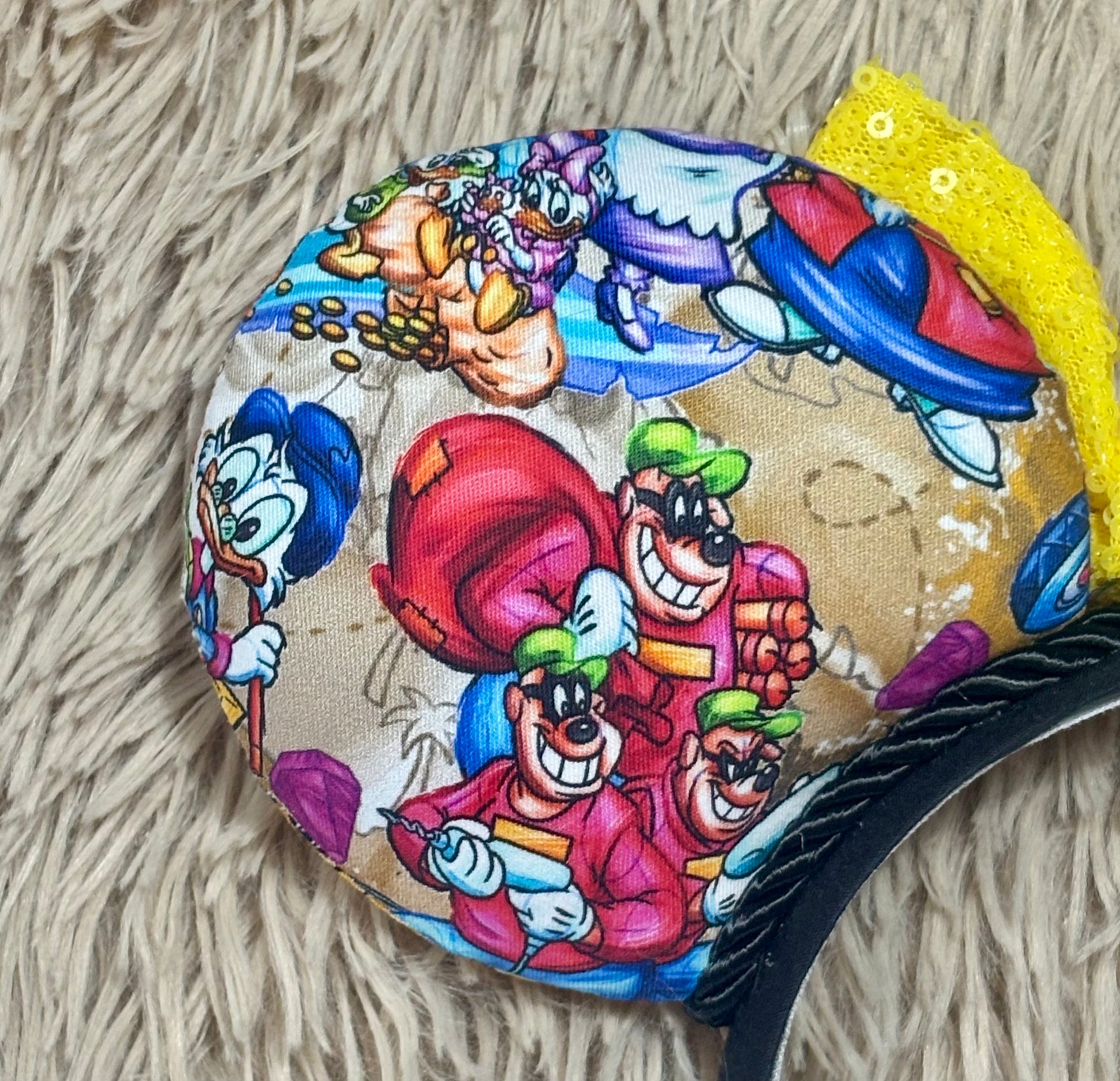 A headband featuring a colorful cartoon print of famous cartoon Duck characters, accented by a large yellow sequined bow in the center.