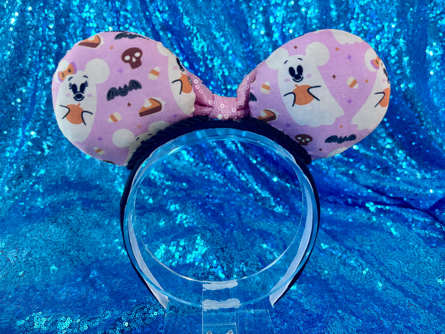 back view with ghosts, bats, skulls and candy corn. Cartoon character ghosts on a mouse ear headband with pink sequin bow shown on a blue glittery background