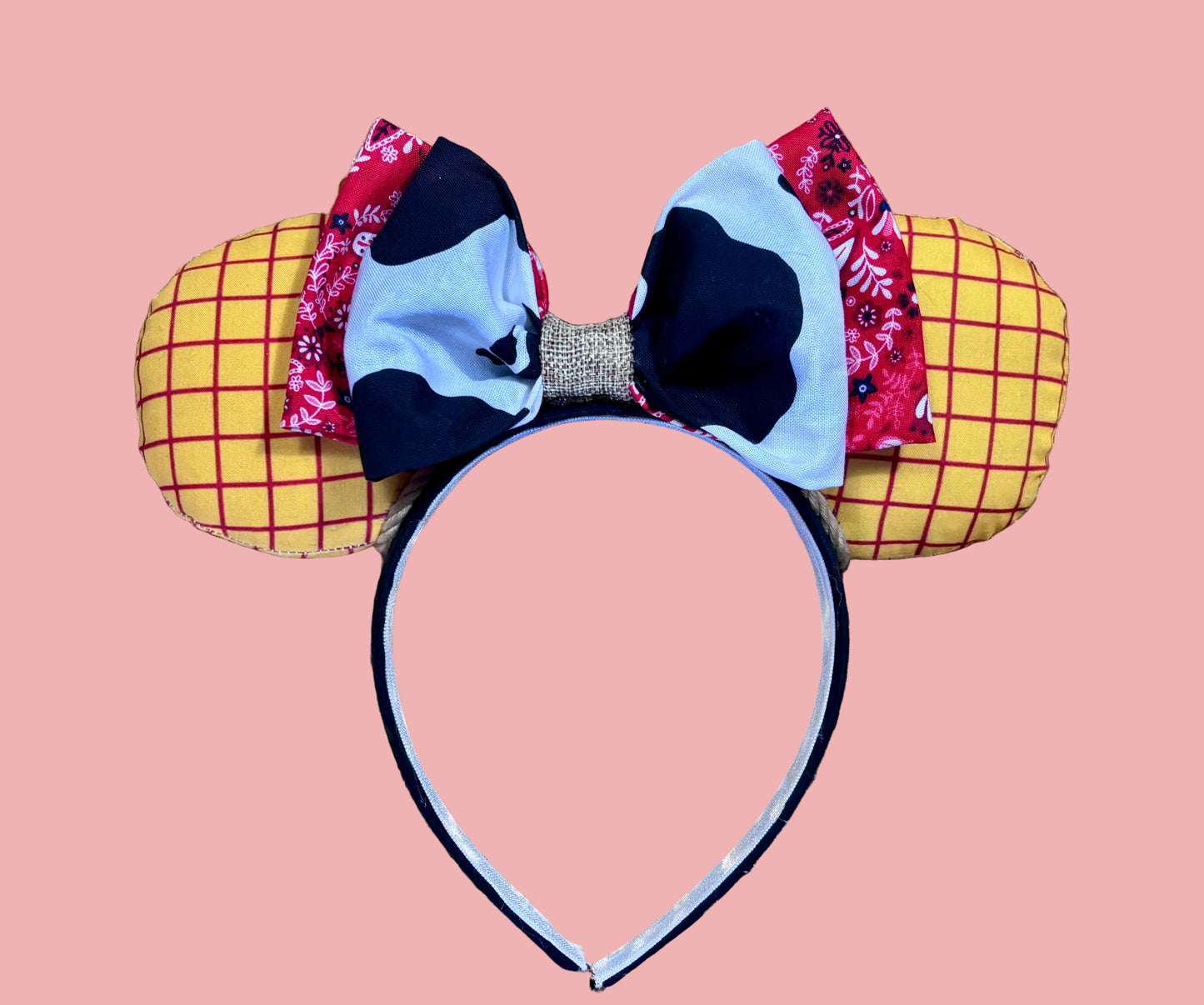 Handmade and ready to ship. Sheriff Woody Inspired mouse ears with the fabric on both the front and back that looks like his shirt. The fabric on the headband is black and is universal sized and fits most. The set has a bandana and cow print layered bow with brown trim along the inner ears to look like rope. Item is shown on a white background.