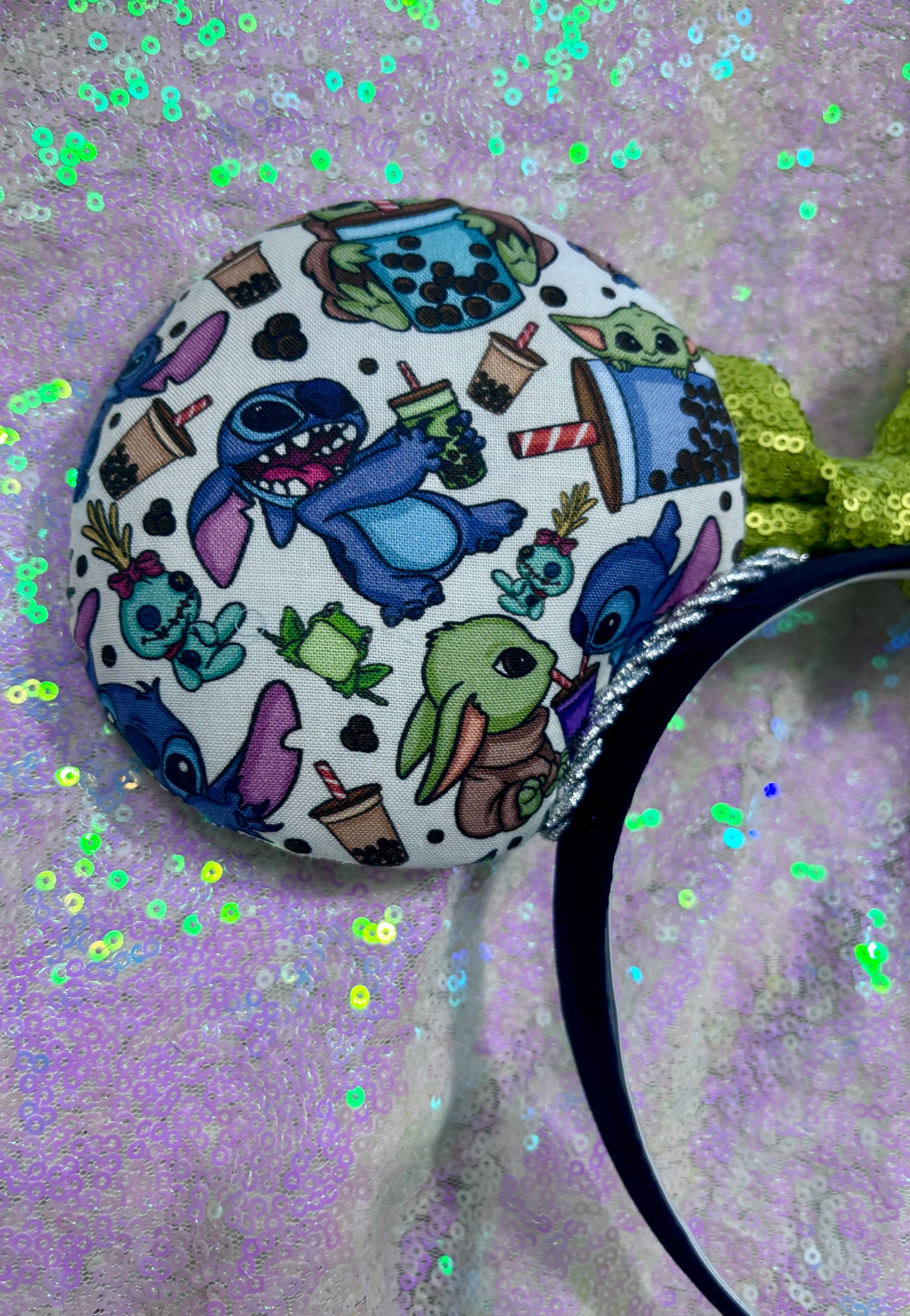 Handmade and ready to ship. Stitch and Baby Yoda are drinking coffee on the front and back with a lime green sequin bow. Shown on a white glitter background.