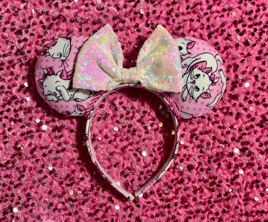 Handmade and ready to ship Marie Inspired Mouse ears with images of her on the front and back of mouse ears shown with a white iridescent sequin bow. The headband has a matching Marie poly cotton fabric and is a universal sized headband.
