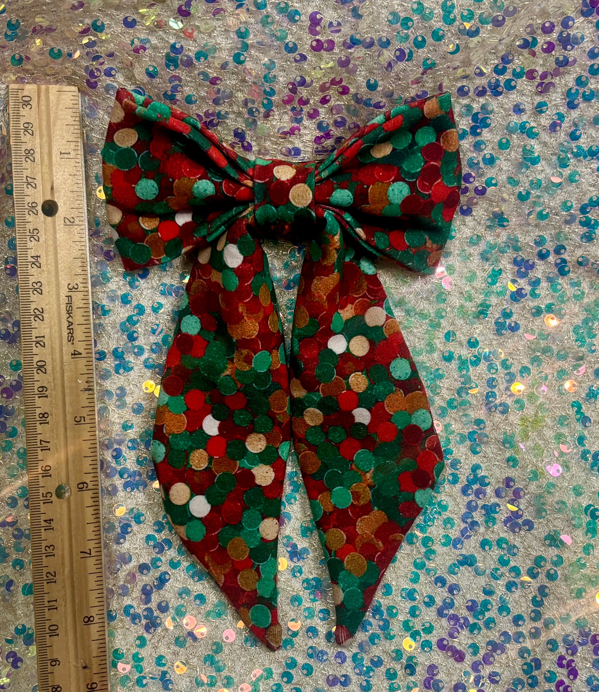 Christmas colors dot bow with a ruler for scale on a glittery background.