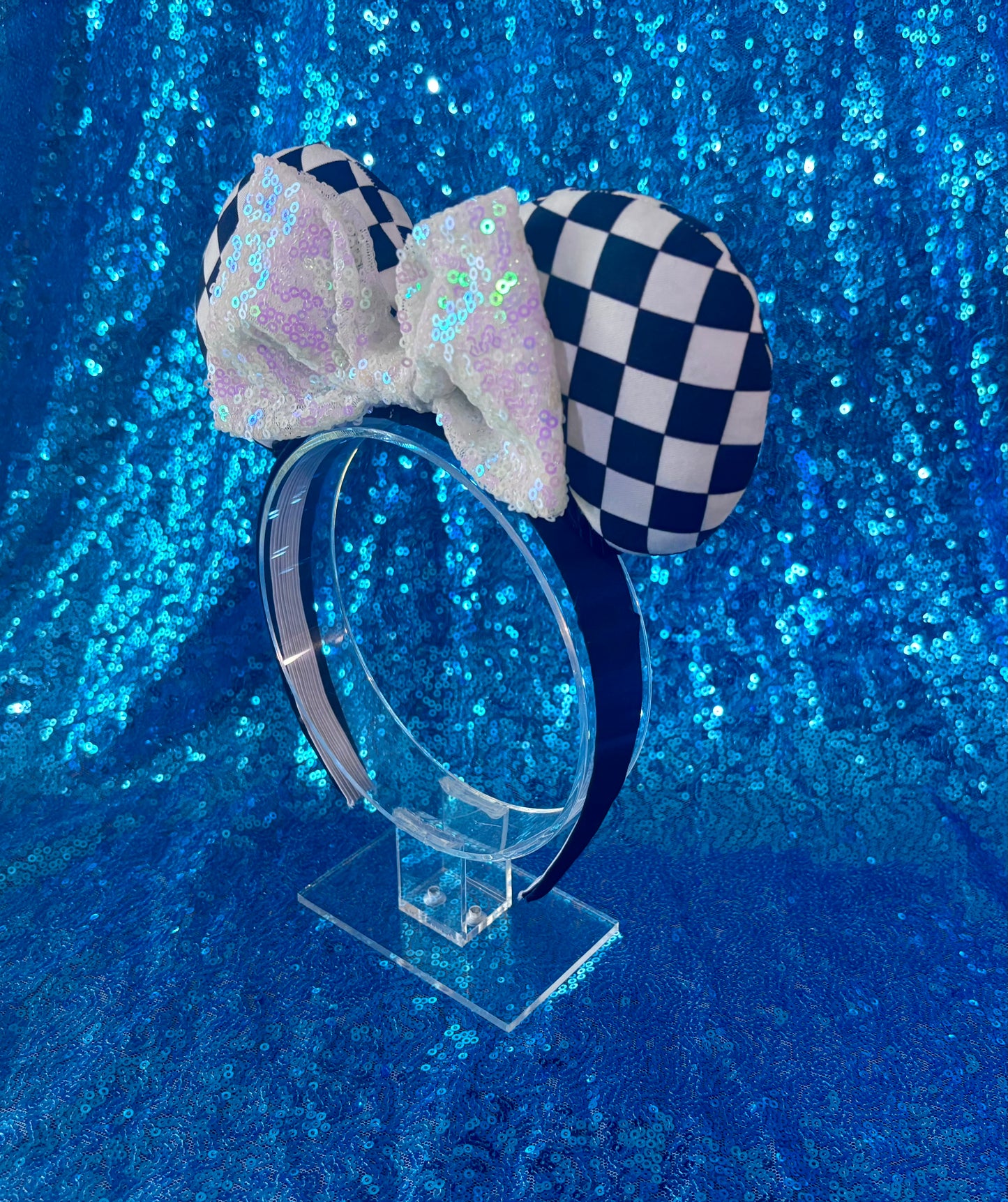 Side view of Checkered bow headband on a clear stand against a blue glittery background