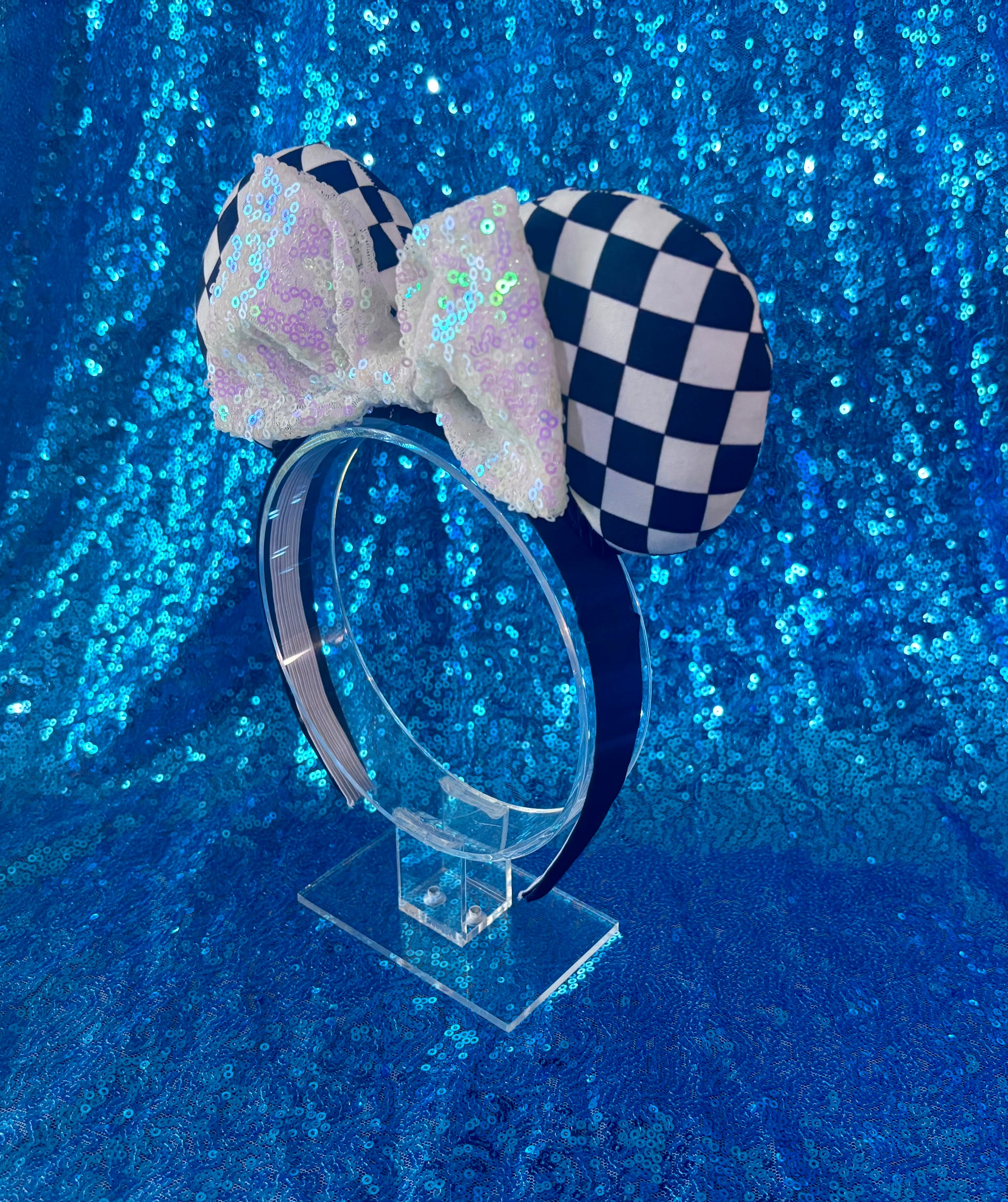Side view of Checkered bow headband on a clear stand against a blue glittery background