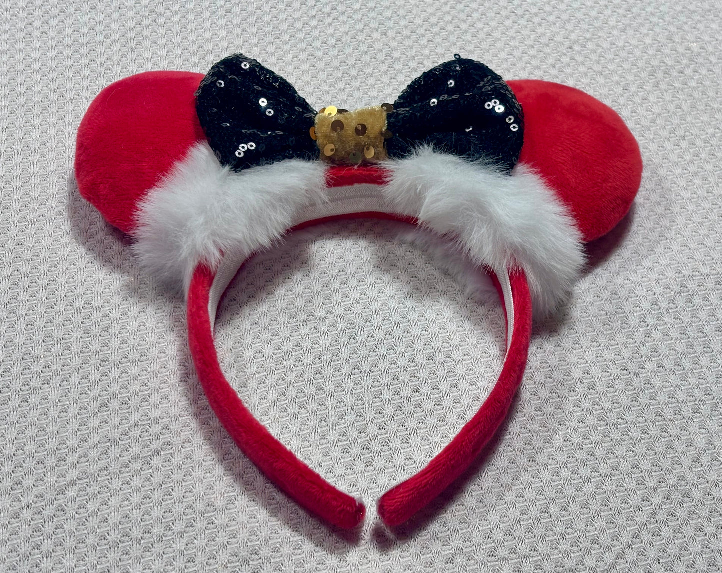 Minnie Mouse ears headband with red plush ears and black bow with gold middle and fluffy white trim on a white background