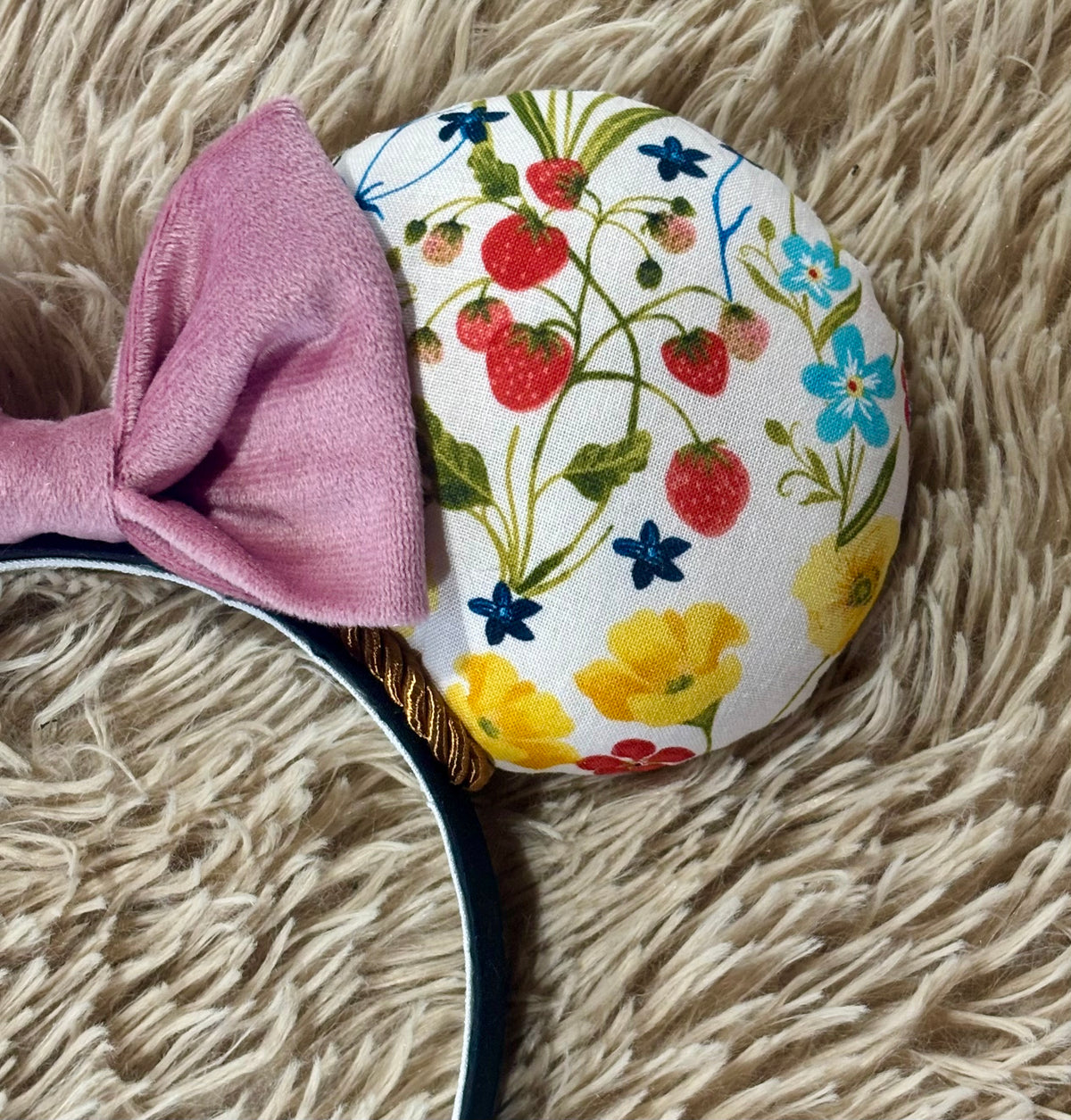 An ear headband accessory featuring a floral-themed print on the ears and a pink velvet bow in the center with copper colored twisted trim along the inner ears.