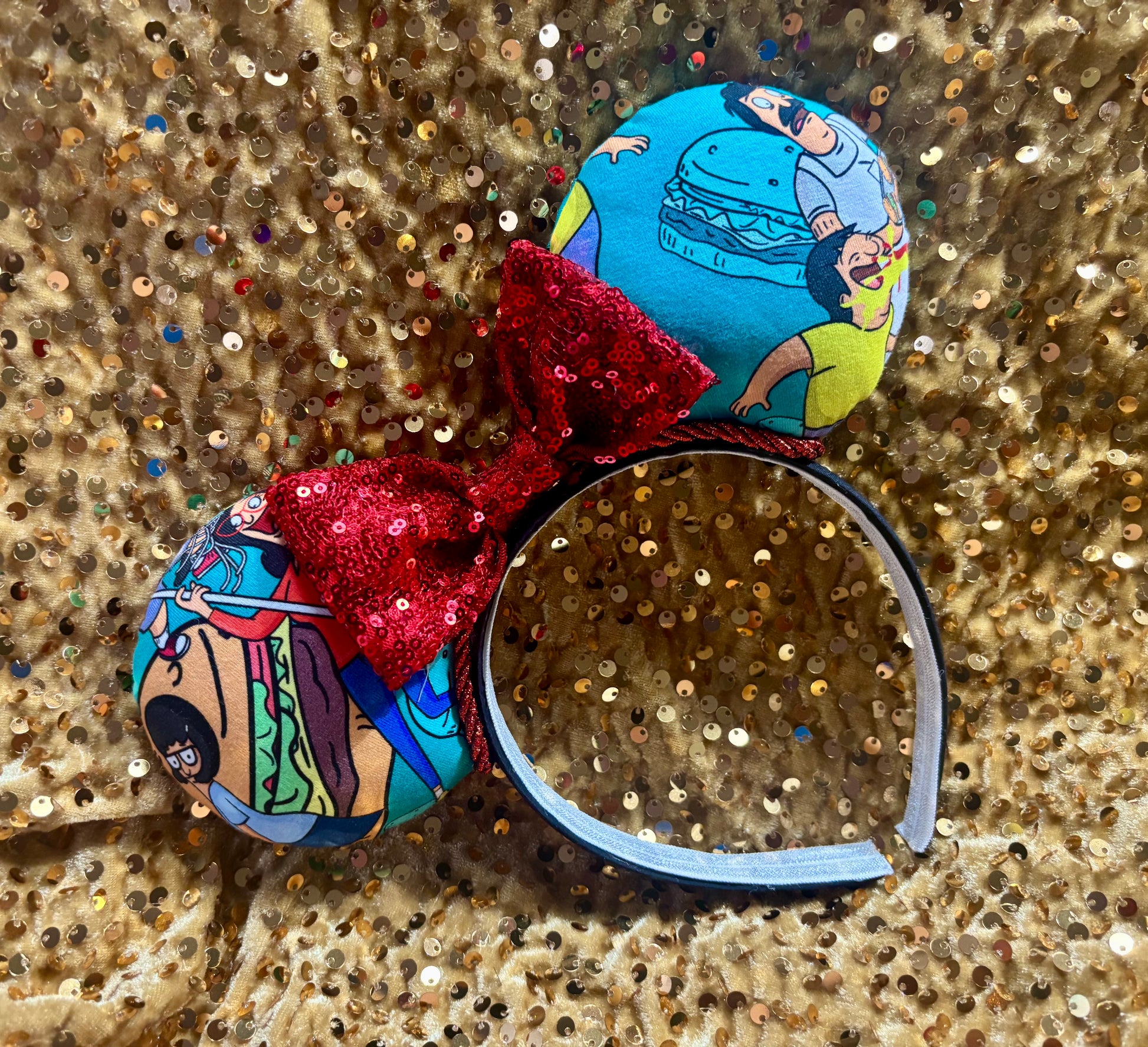 Colorful headband with cartoon character buttons and a red bow on a glittery gold background.