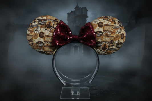 Tot themed Mouse ears with gold and red design and a burgundy red sequin bow. Shown on a green satin background
