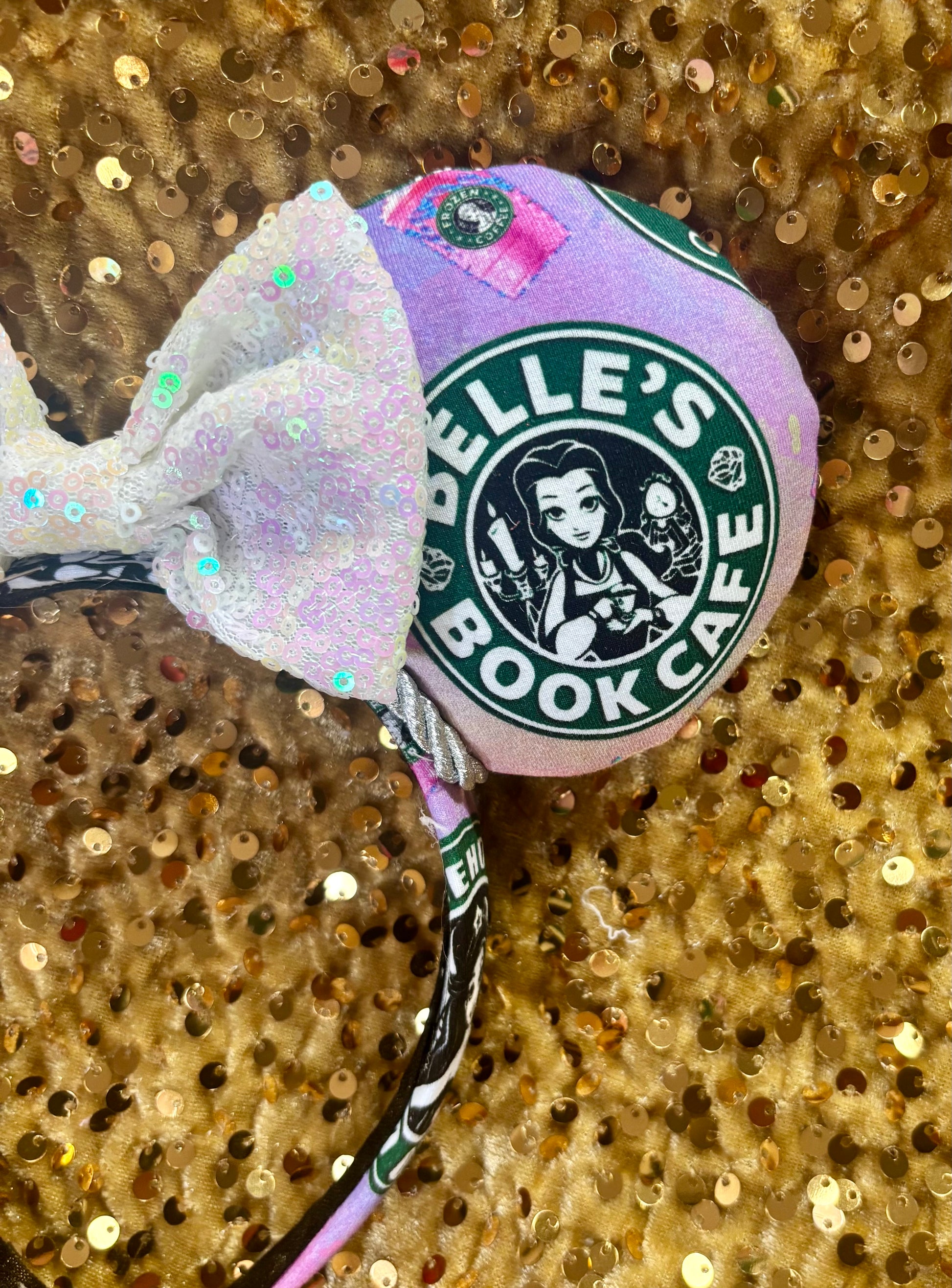 Front view of other side of mouse  ears showing ‘Belle's Book Cafe' branding on a glittery gold background