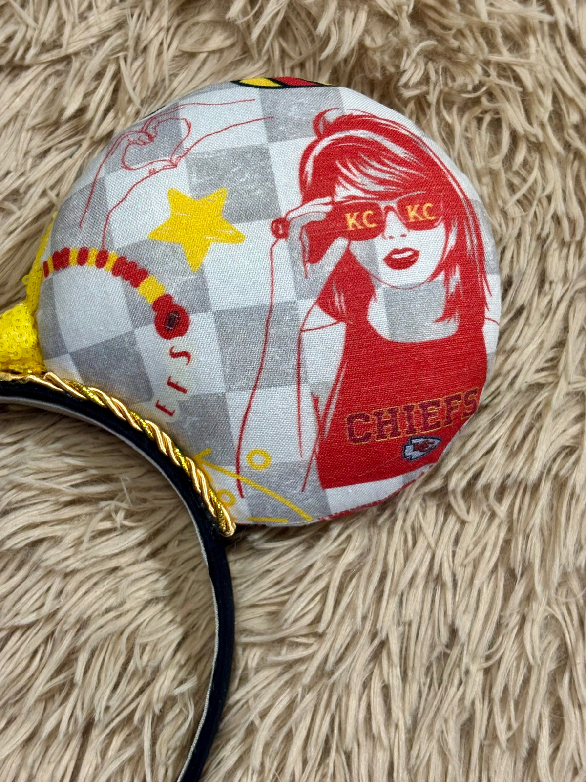 An ear headband featuring a bright yellow sequined bow. The set has TS and Chiefs images on it. Set on a universal sized headband.