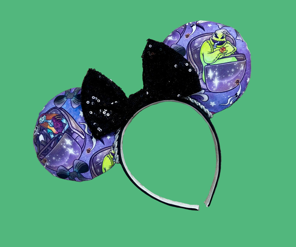 An ear headband accessory with a black sequined bow, featuring a purple HM and NBC themed print with a cartoon character in a buggy.