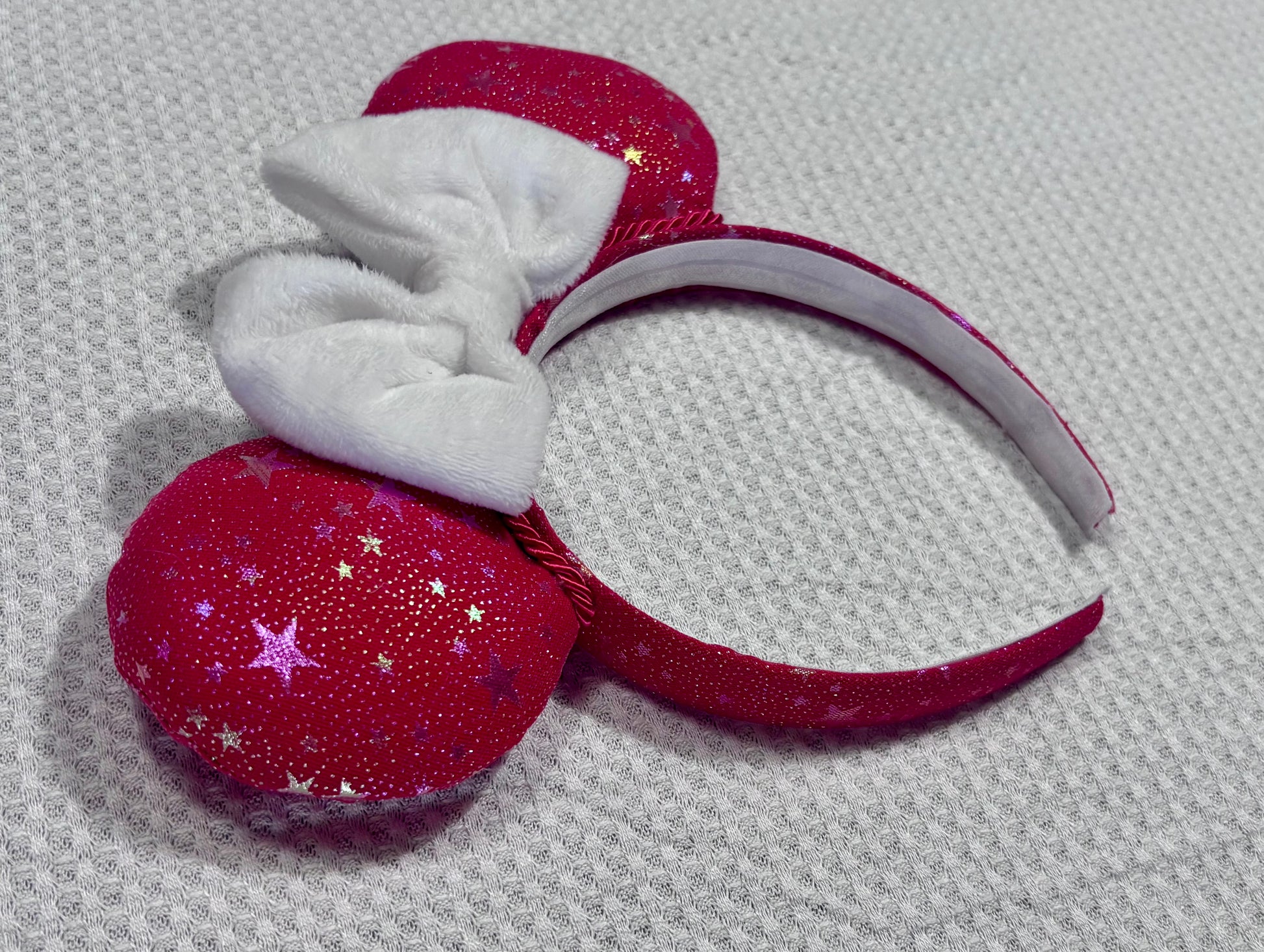 Handmade and ready to ship red mouse ears with iridescent stars on both the front and back along with the headband as well. The set has a white soft bow. Item is shown on a white background.