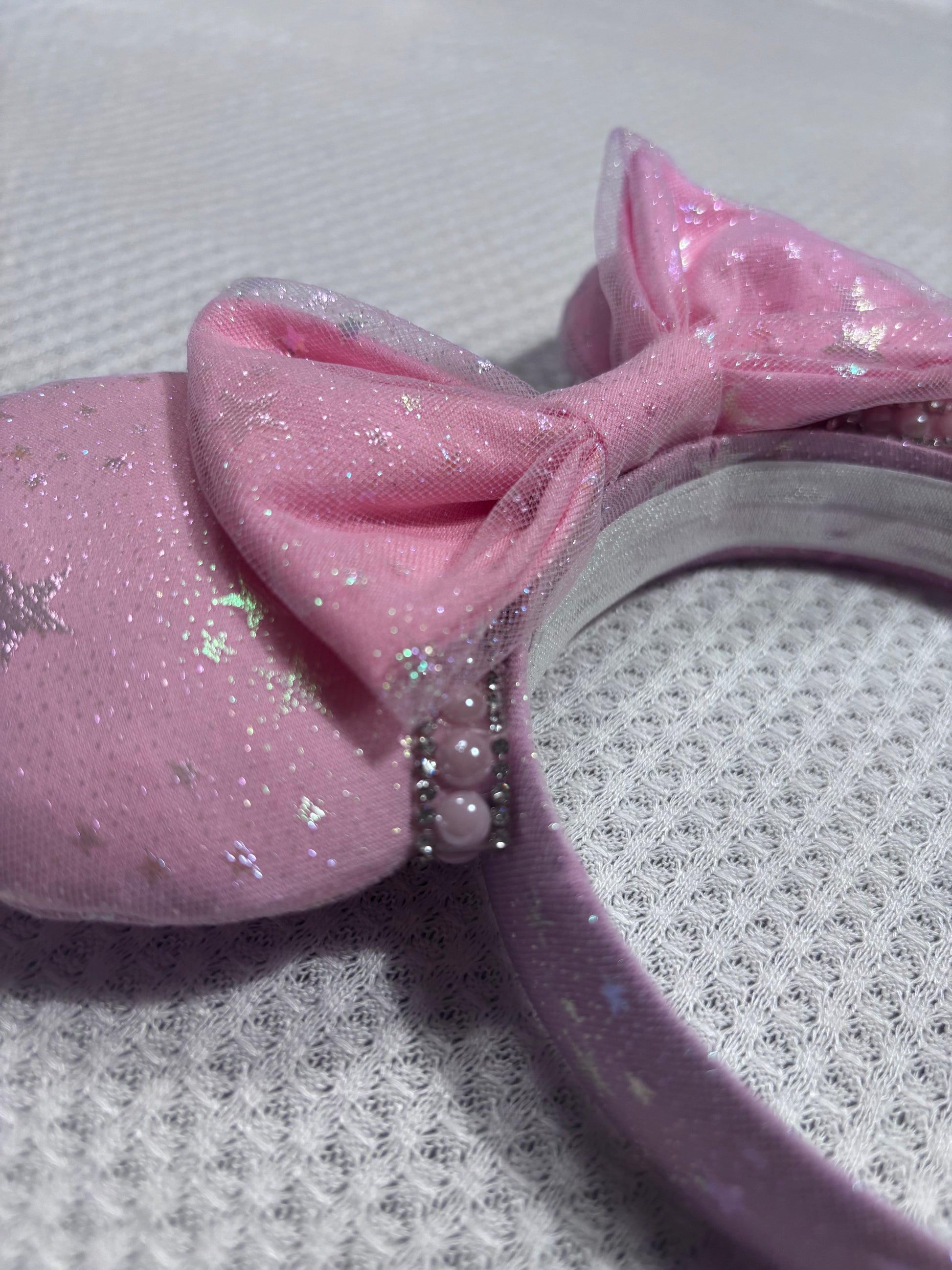 Close up of the pink and silver gemstone trim. Handmade and ready to ship Pink Sparkling Iridescent fabric on pink to make mouse ears with the fabric on both the front and back along with the headband the is universal sized and fits most. The set has a matching bow, but you can request any sequin color in your order and I'll attach it. Item is shown on a white background.