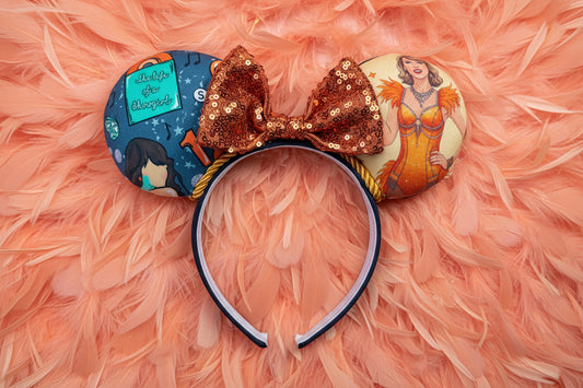Decorative mouse ears inspired by TS12 on a black headband with a orange sequin bow and character designs. Shown on a pink feather background