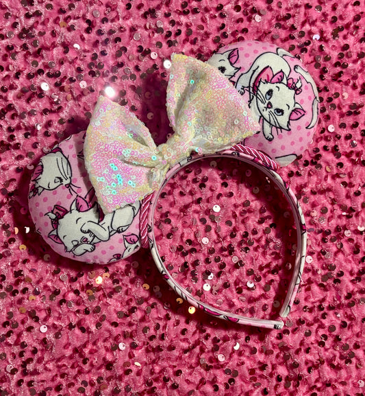 Handmade and ready to ship Marie Inspired Mouse ears with images of her on the front and back of mouse ears shown with a white iridescent sequin bow. The headband has a matching Marie poly cotton fabric and is a universal sized headband.