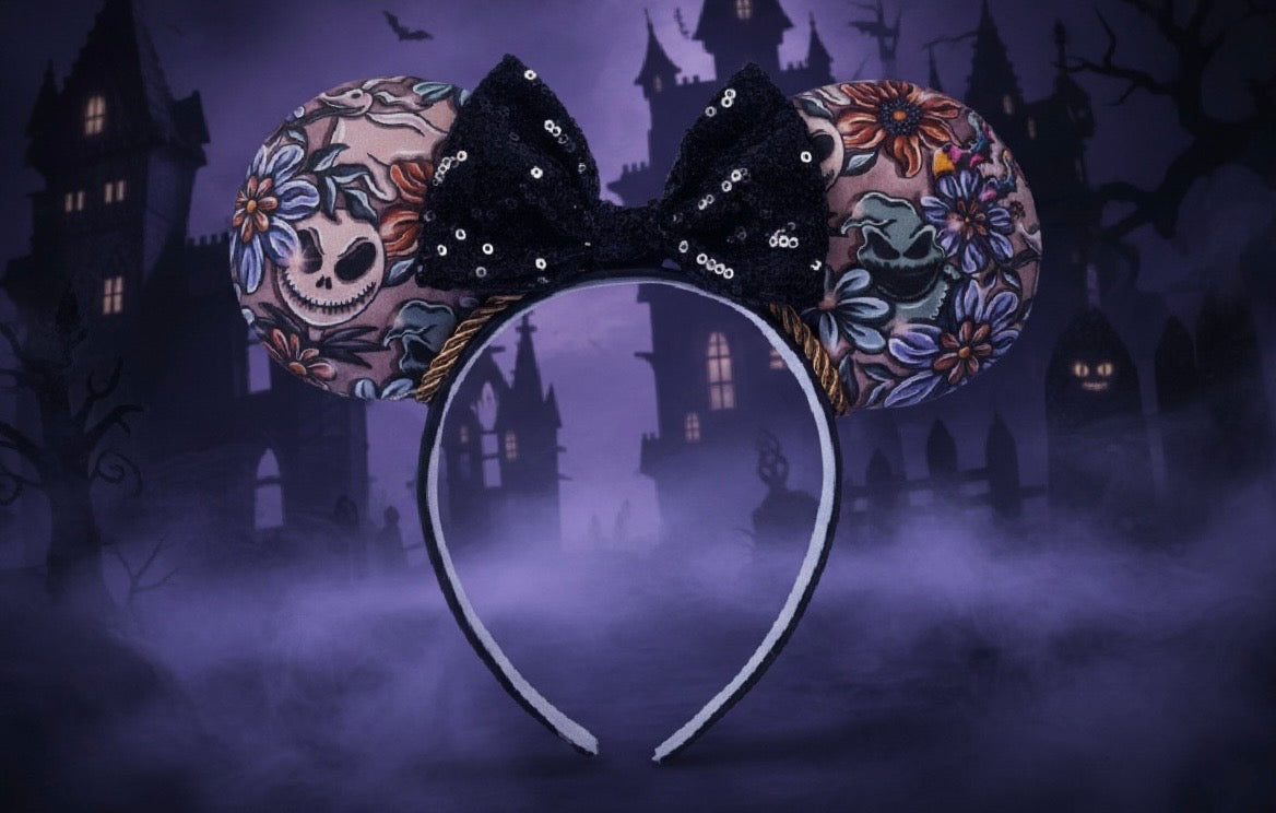 Halloween-themed NBC mouse ears on a black headband and black sequin bow and twisted trim. Shown with floral and skull designs against a spooky castle background.