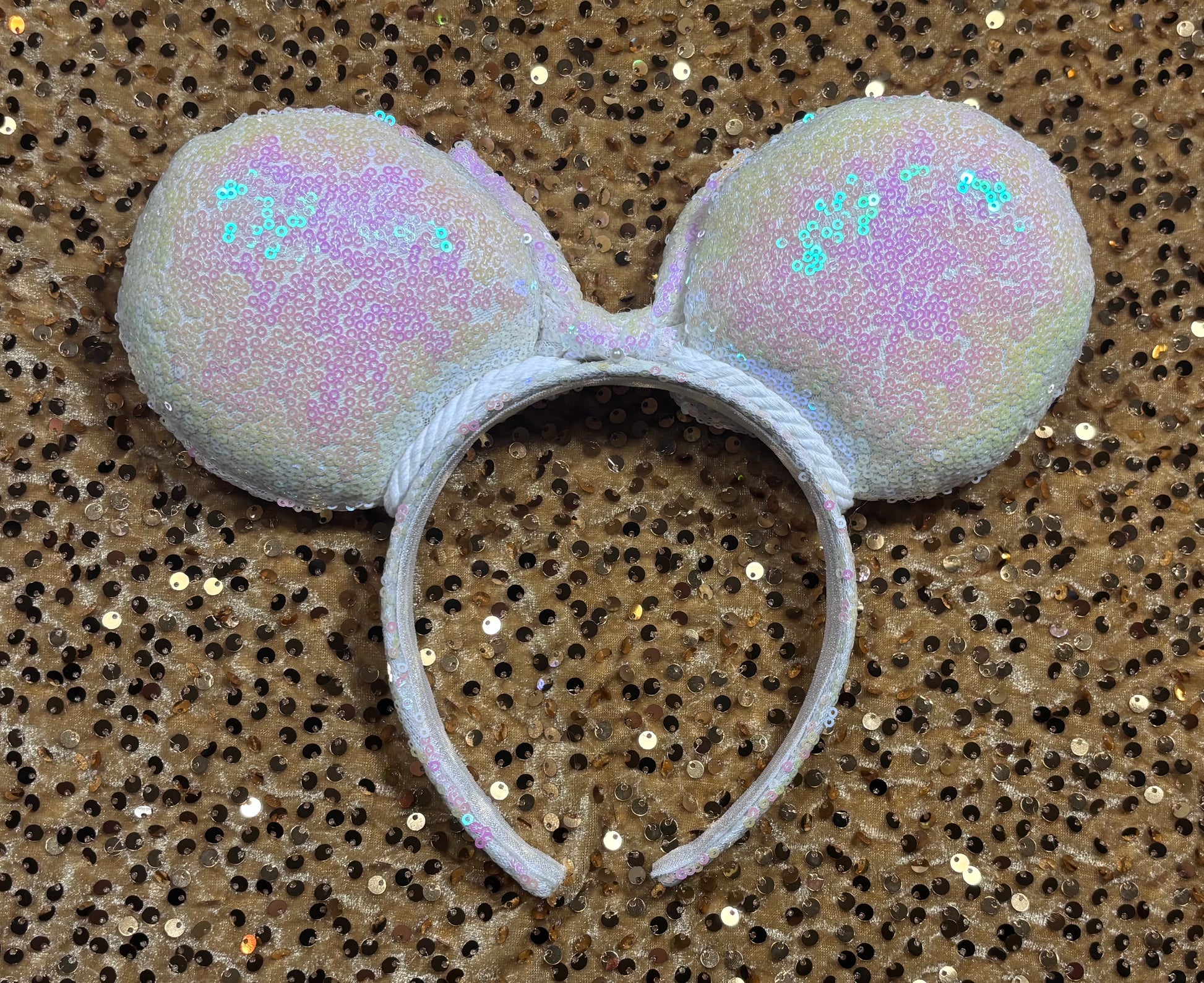 White Iridescent mouse ears with the fabric on both the front and back. The fabric is on the headband as well and is universal sized and fits most. The set has a matching iridescent bow sequin bow. Item is shown on a gold sequin background. Back view of mouse ears.