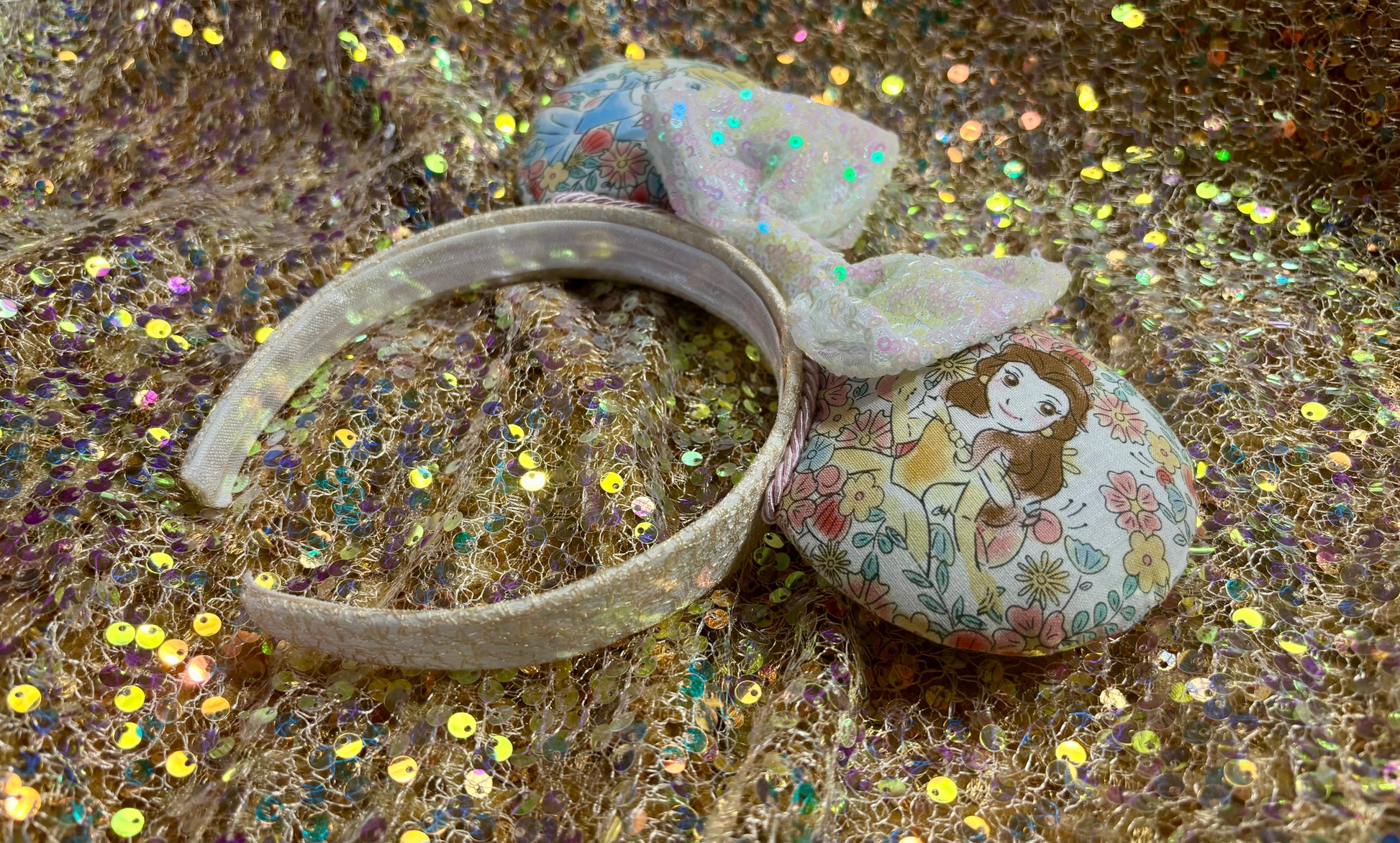 Handmade and ready to ship Pretty Princess Mouse ears with Cinderella and Belle shown on the fabric with a white iridescent bow. The headband has a white shimmery fabric and is a universal sized headband.