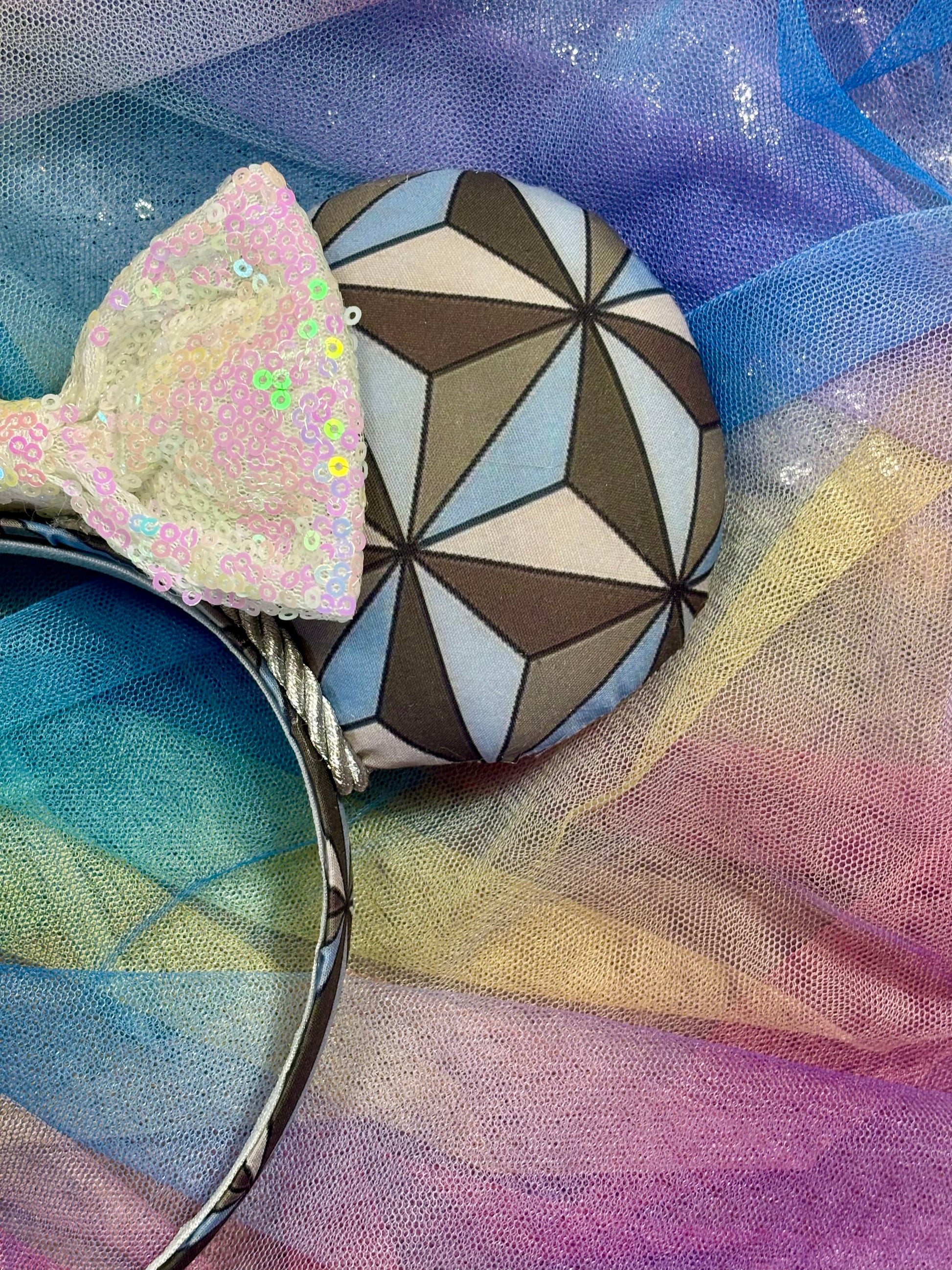 Mouse ear headband with a geometric design inspired by Spaceship Earth ride and a white iridescent bow on a colorful background. Showing the other front side of mouse ear.