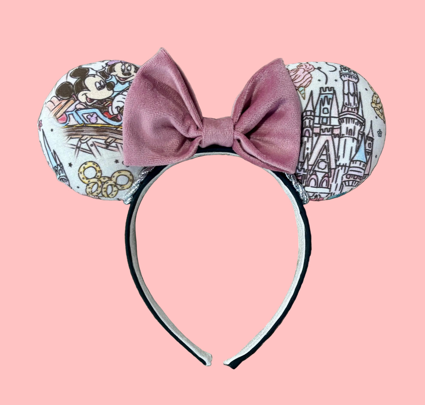 A pair of handmade ear headbands with a large dusty pink velvet bow, featuring printed park themed patterns on the ears and resting on a beige faux fur surface.
