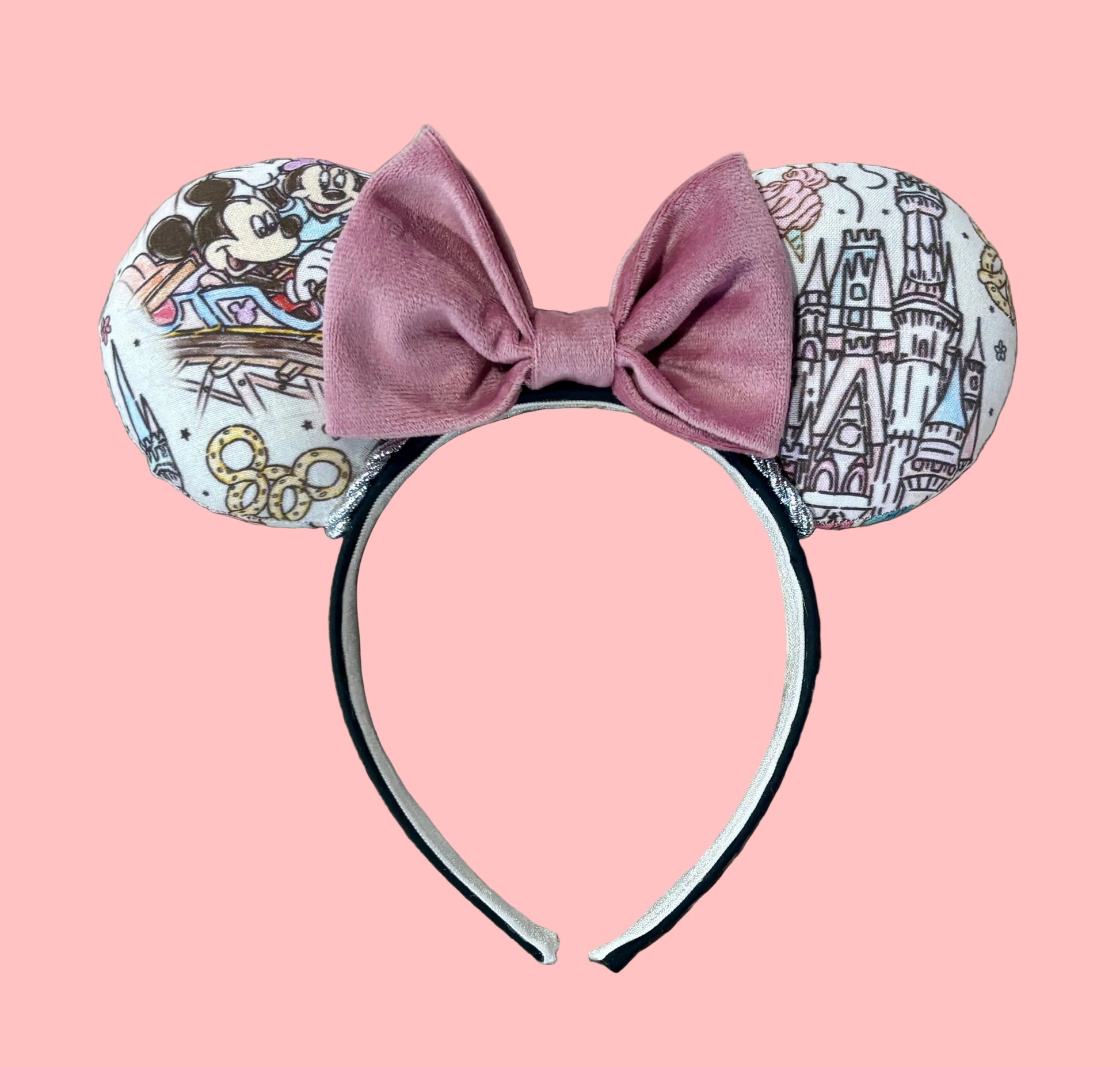 A pair of handmade ear headbands with a large dusty pink velvet bow, featuring printed park themed patterns on the ears and resting on a beige faux fur surface.